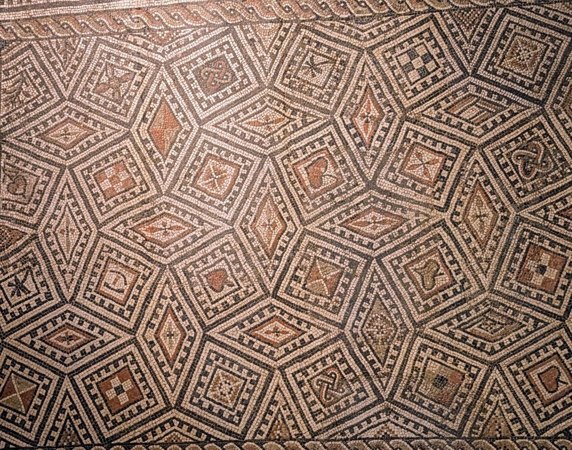 Kleinteiliges Mosaik aus farbigen Glassteinchen mit einem Muster aus Rauten und Vierecken, die einen dreidimensionalen Effekt erzielen.