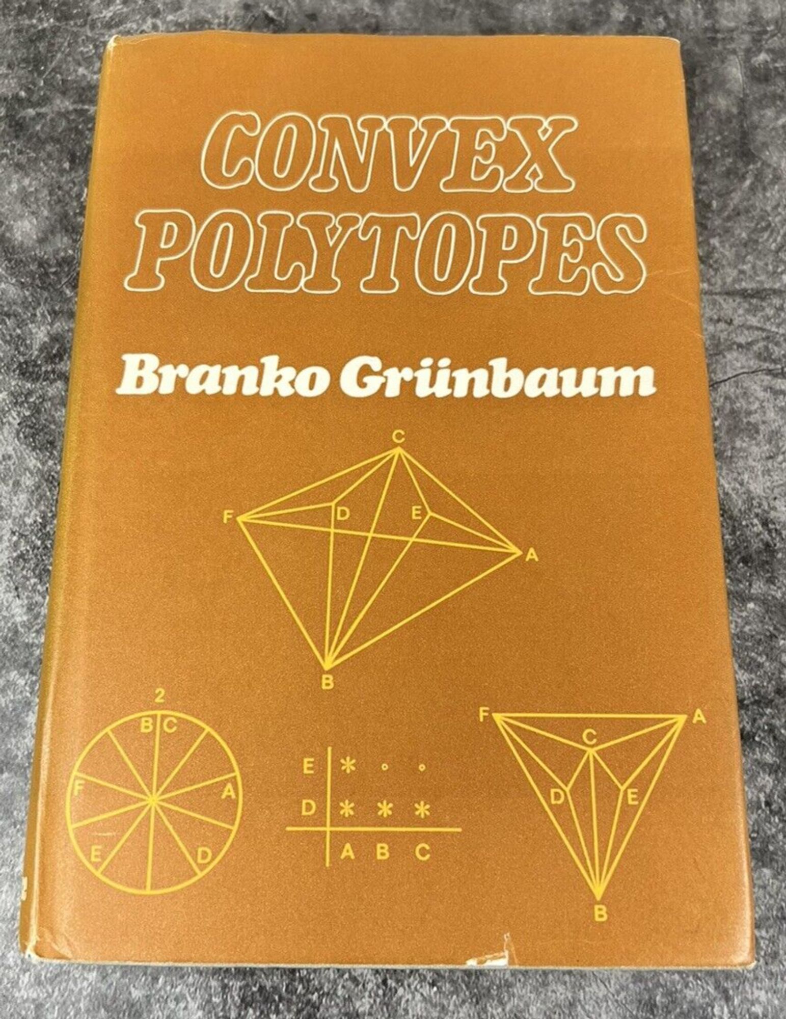 A dank early edition of Convex Polytopes by Branko Grünbaum. Lettering is sort of bubble soft italicized curvy serif and there are an assortment of convex polytopes (a sort of multidimensional polygon). Mustard with yellow and white