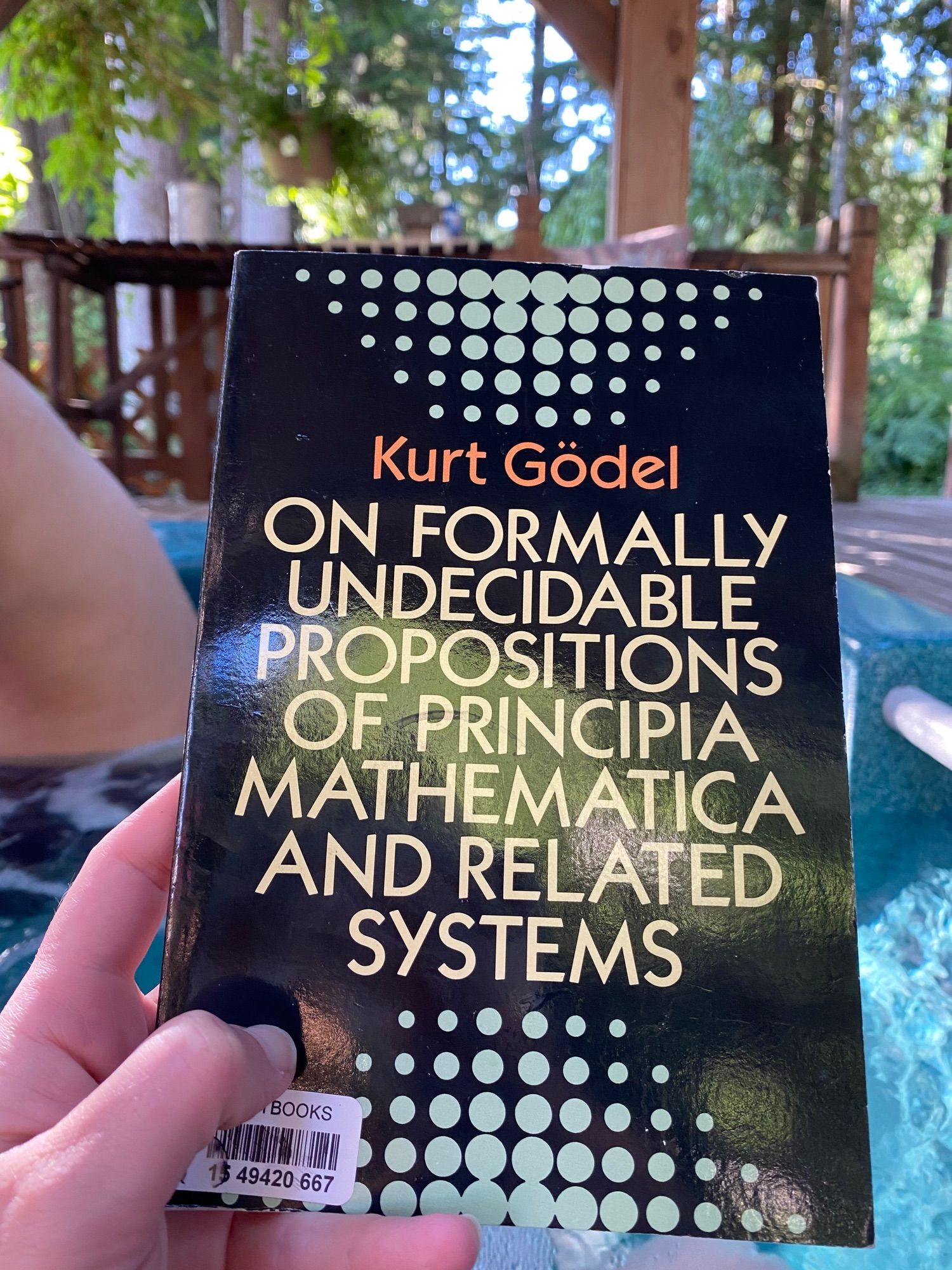 A photo of On Formally Undecidable Propositions of Principia Mathematica and Related Systems by Kurt Gödel, Dover edition. Nice block lettering framed by a reflected motif of a pyramid of dots of decreasing size. Black background, dots are pale blue. Lettering & name are in yellow and orange. Notably this is being perused in a hot tub.