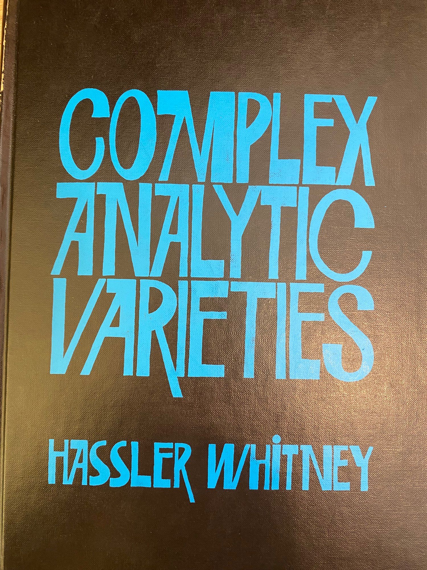 A math book called complex analytic varieties by hassler (what a name!) Whitney. Black background, soft robin blue lettering whose shape is telling me this book is not only gonna have math but almost certainly 1960s sitcom style bawdy shenanigans