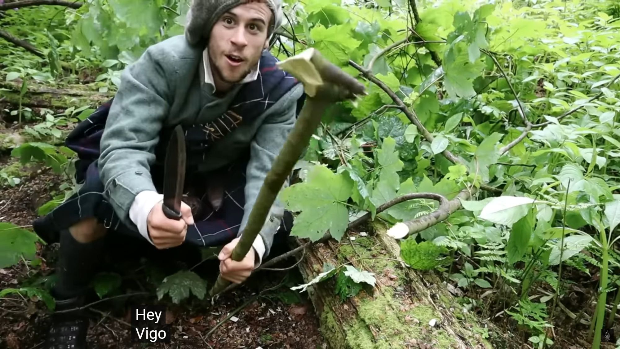 Tom Langhorne from YouTube channel Fandabi Dozi, dressed in historical Scottish Highland dress and deep in the woods, demonstrating the cudgel, or celtic shillelagh, he fashioned from a fallen rowan branch using nothing but his dirk in just a minute or two, trying to re-enact the Campbells fighting off the McMartin ambush described in the video from which the screencap was pulled.