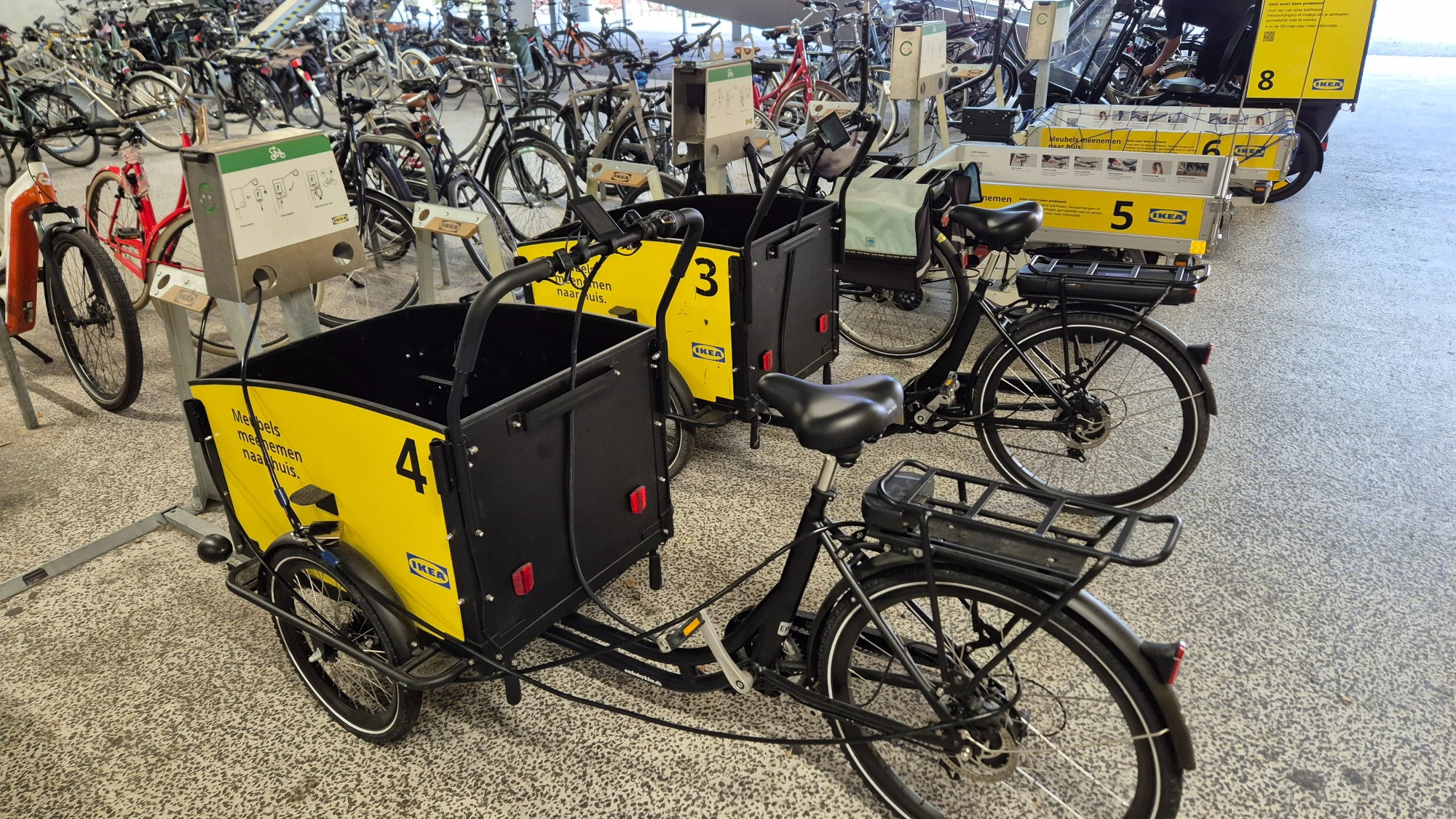 Photo of two IKEA cargo bikes. Behind them are two IKEA e-bike trailers and a covered IKEA cargo bike.