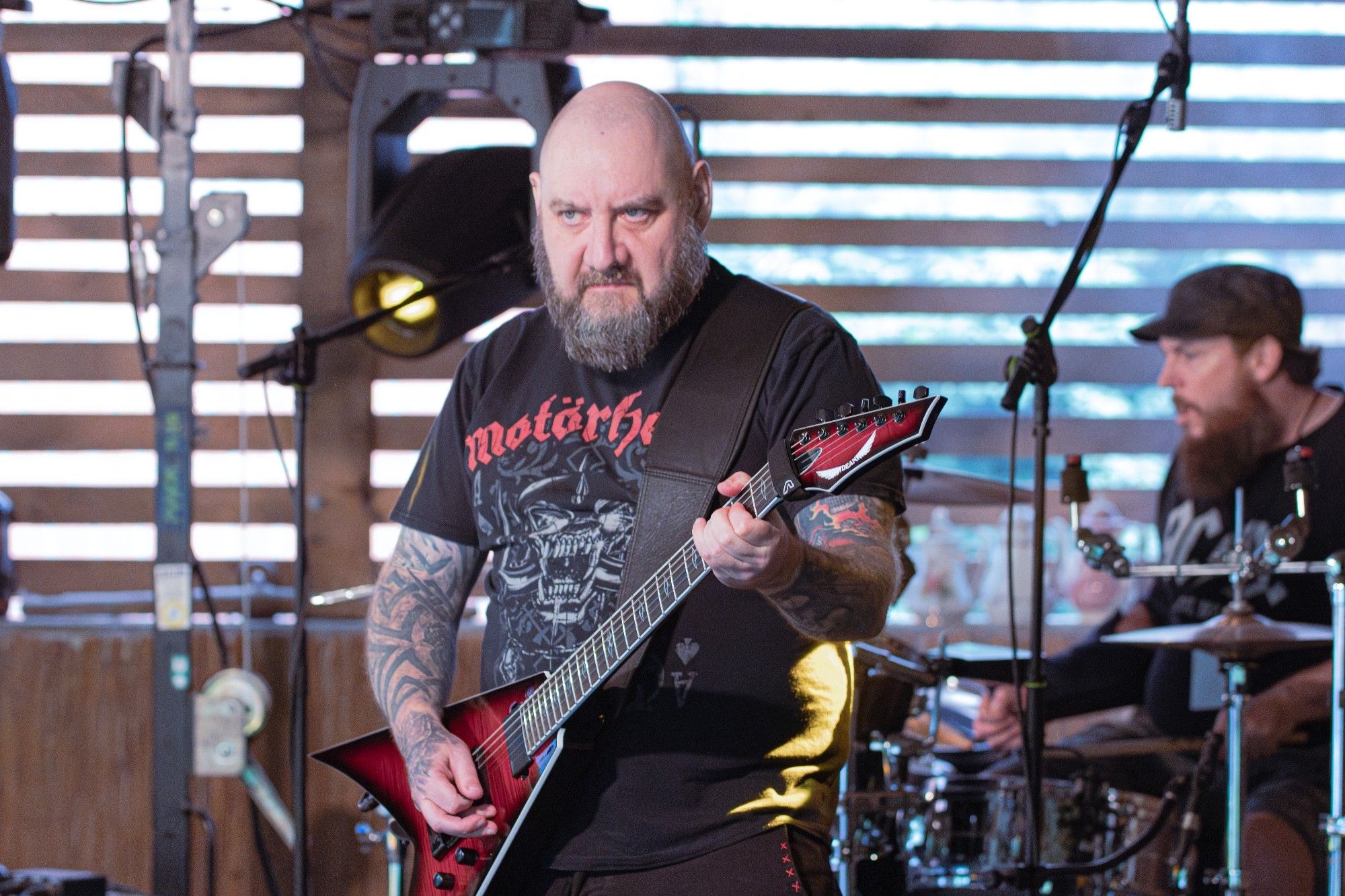 Foto von mit beim Konzert. Ich mit Glatze, Bart, Motörhead Shirt und redburst Flying V. Rechts im Hintergrund unser Drummer am Schlagzeug mit Kappe und Bart.