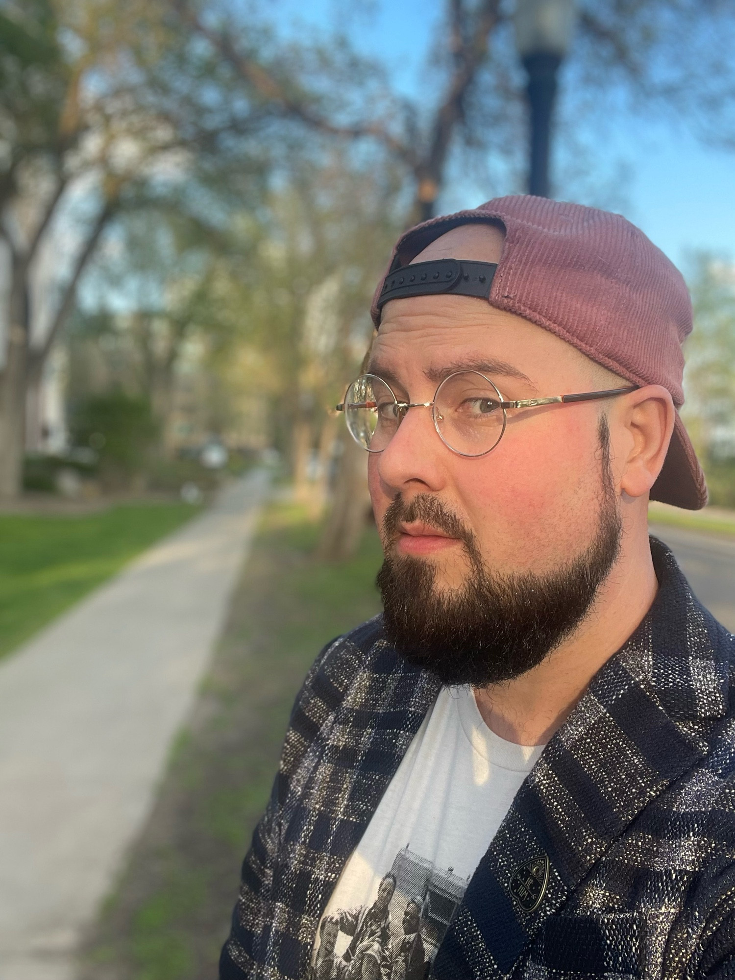 A white man with a pink cap, white tee with the cast of Twister, a blazer, beard and glasses.