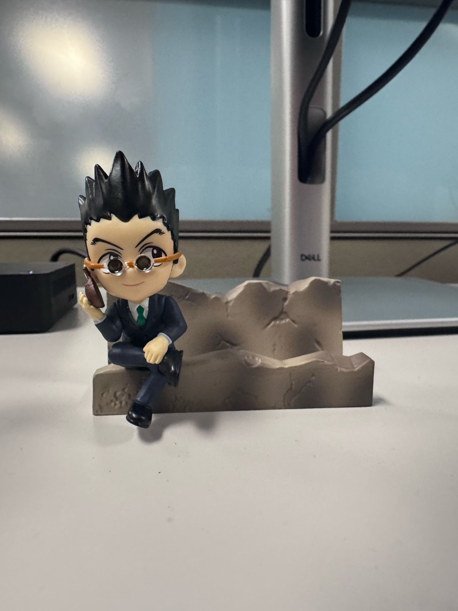 A phone holder that’s shaped like a little bit of rubble. A squished down version of Leorio from Hunter Hunter is sitting on the rubble with his legs crossed. He’s taking a call on his little beetle phone.