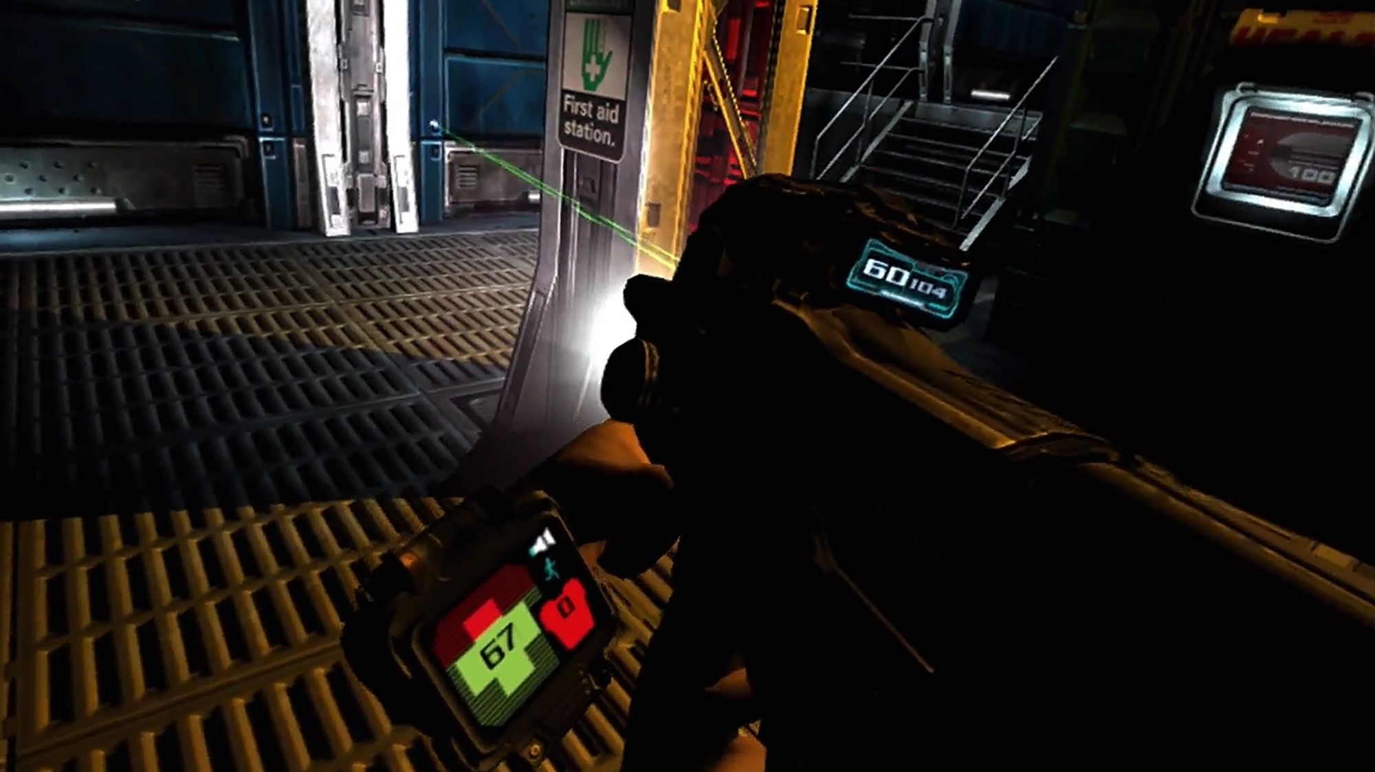 The marine protagonist examines his gun from the first person perspective near a medical station. He is holding a machine gun. The ammo counter reads fully loaded, with 60 rounds in the clip and 114 in reserve. His wrist mounted AVD displays 67 health, 0 armor, low flashlight battery, and full stamina. A nearby sign features a drawing of a hand with a finger injury and reads "First Aid station.", and the health terminal has a full 100.