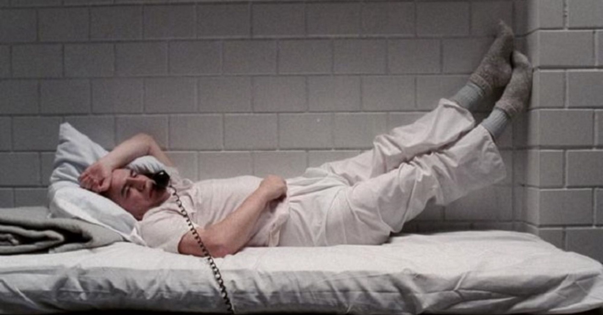 A still from Manhunter of Brian Cox as Hannibal Lekter lounging around his cell, talking on the phone.