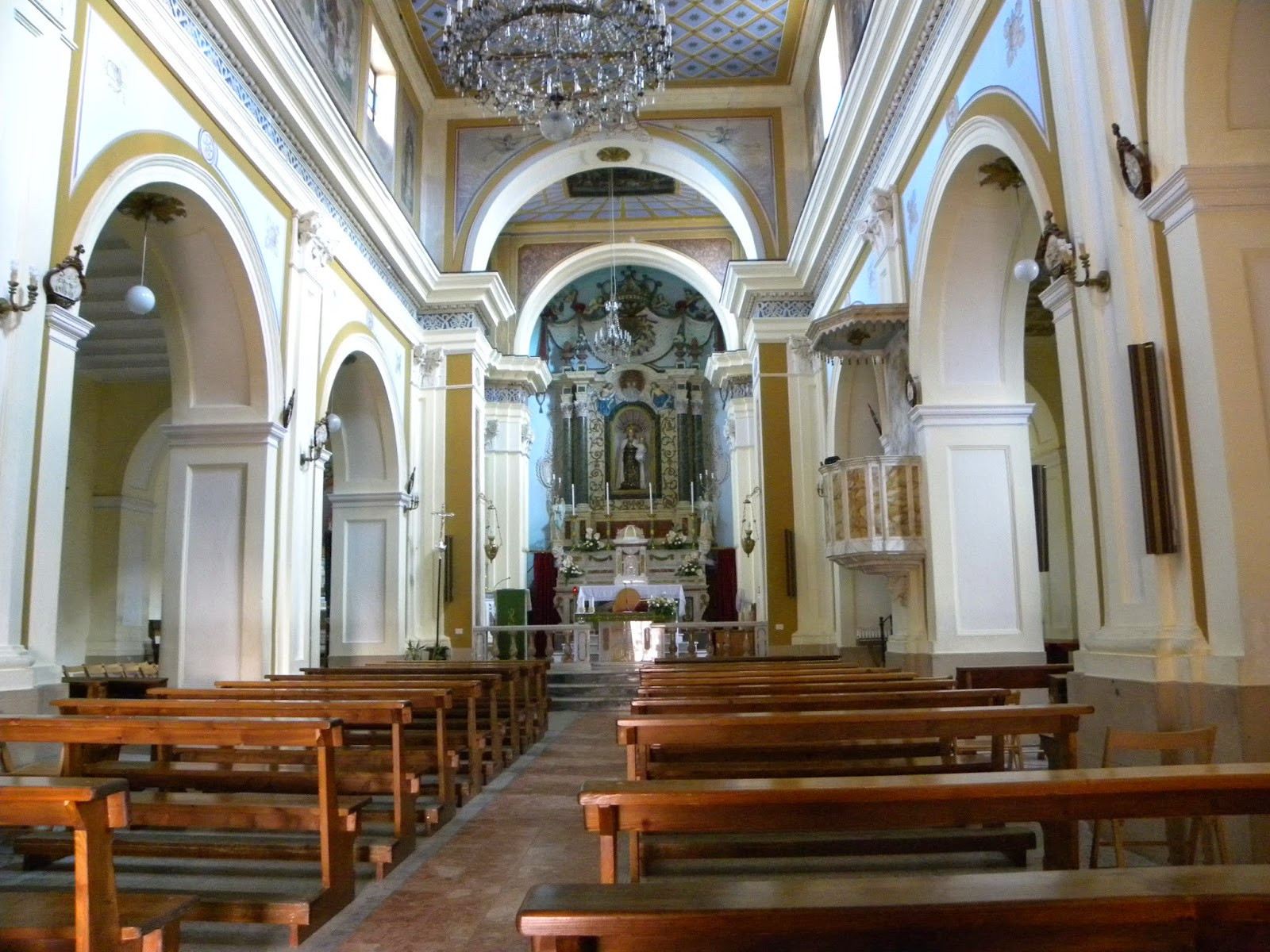 interior of church looking down main aisle towards the altar where there is a statue of Our Lady of Mt Carmel. a chandelier hands from the ceiling of the nave. There is a pulpit built into the wall on the right. 