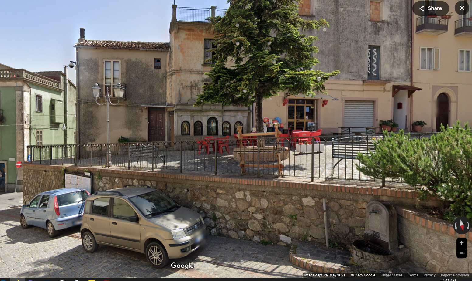 google maps view of the other side of th epiazza with a tree and bushes, some benches, and shope.