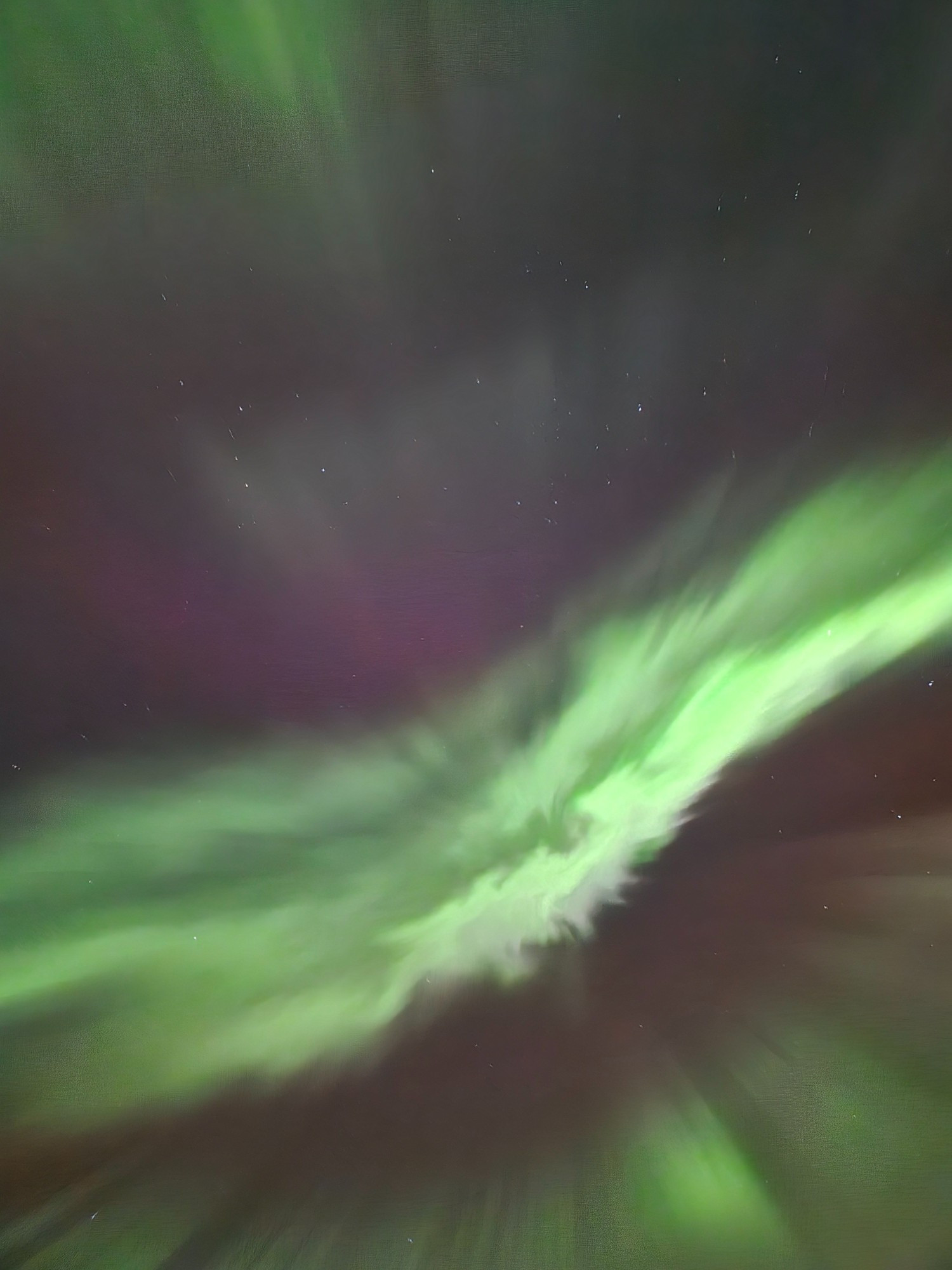 A vivid green aurora band stretches across the image from edge to edge. The center is multiple lines of different shades of green, fading into a dark pink and additional green curtains. The photo was taken pointing at the sky's apex.