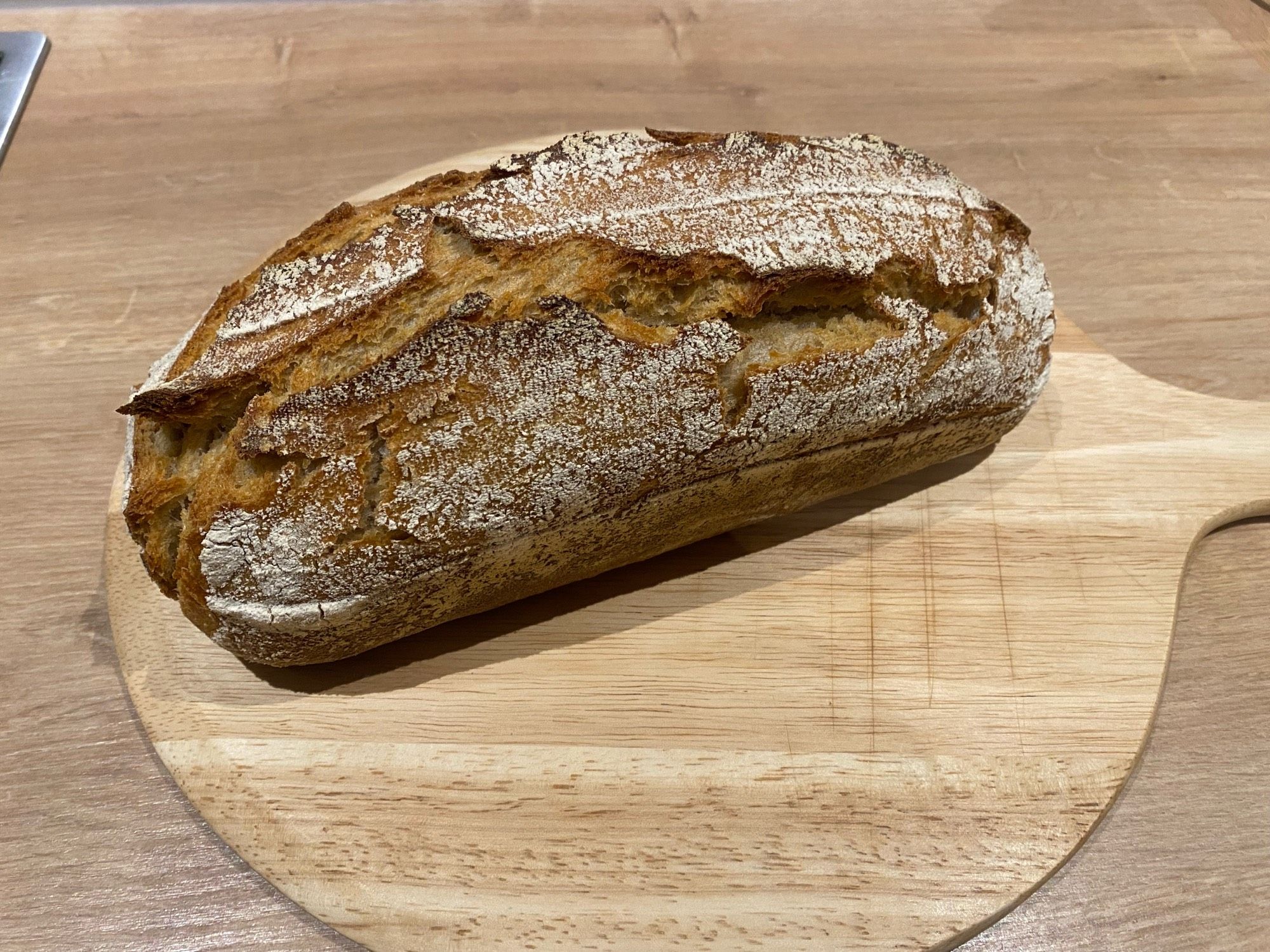 Ein frisch gebackenes Brot auf einem runden Schneidebrett.