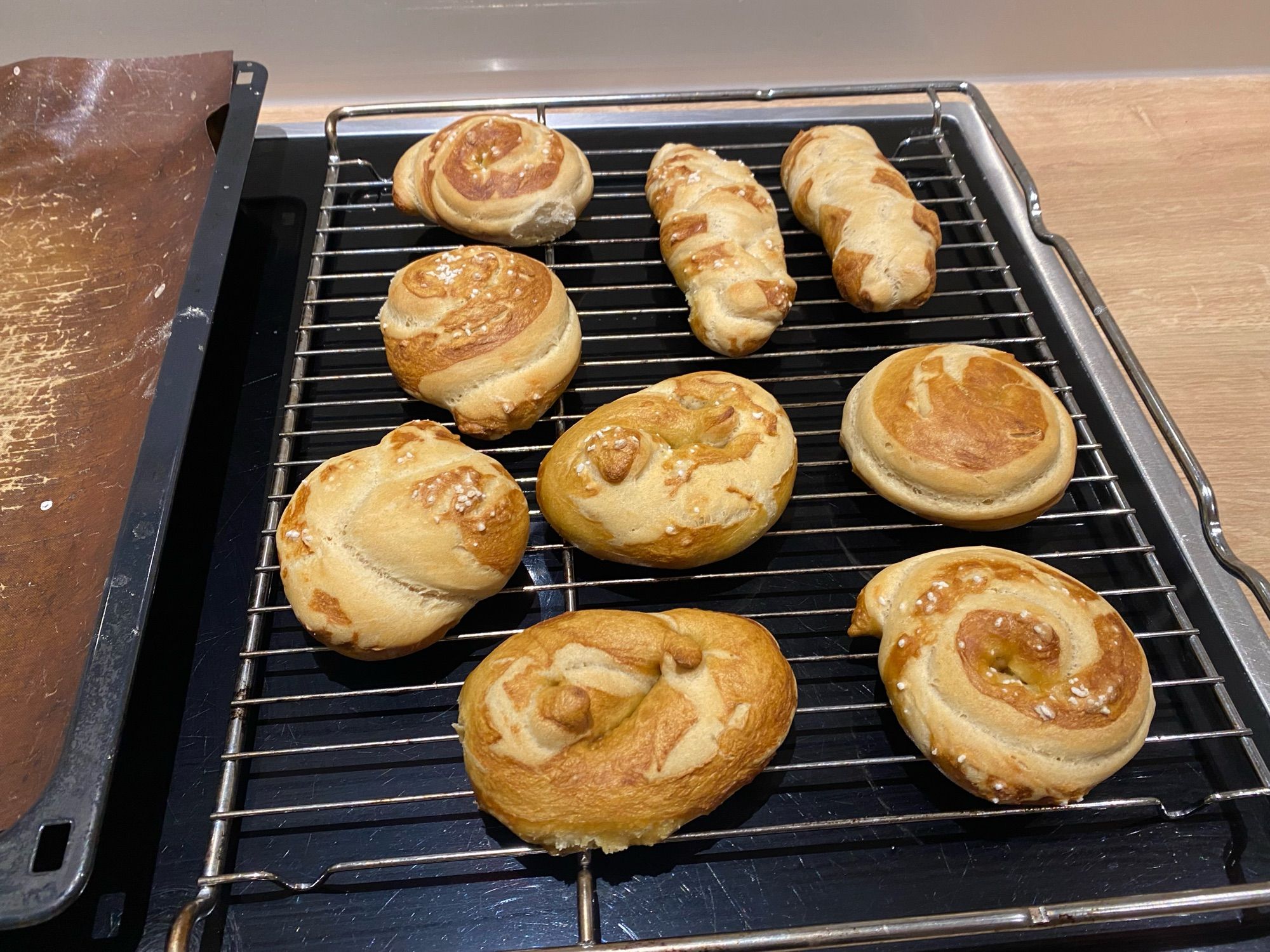 Neun selbst- und frischgebackene Laugenteile in verschiedenen Formen auf einem Rost zum Abkühlen.