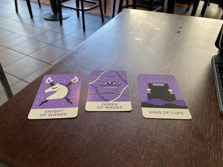 Knight of Wands, Queen of Wands, and King of Cups tarot reading on a Cafe Nero table