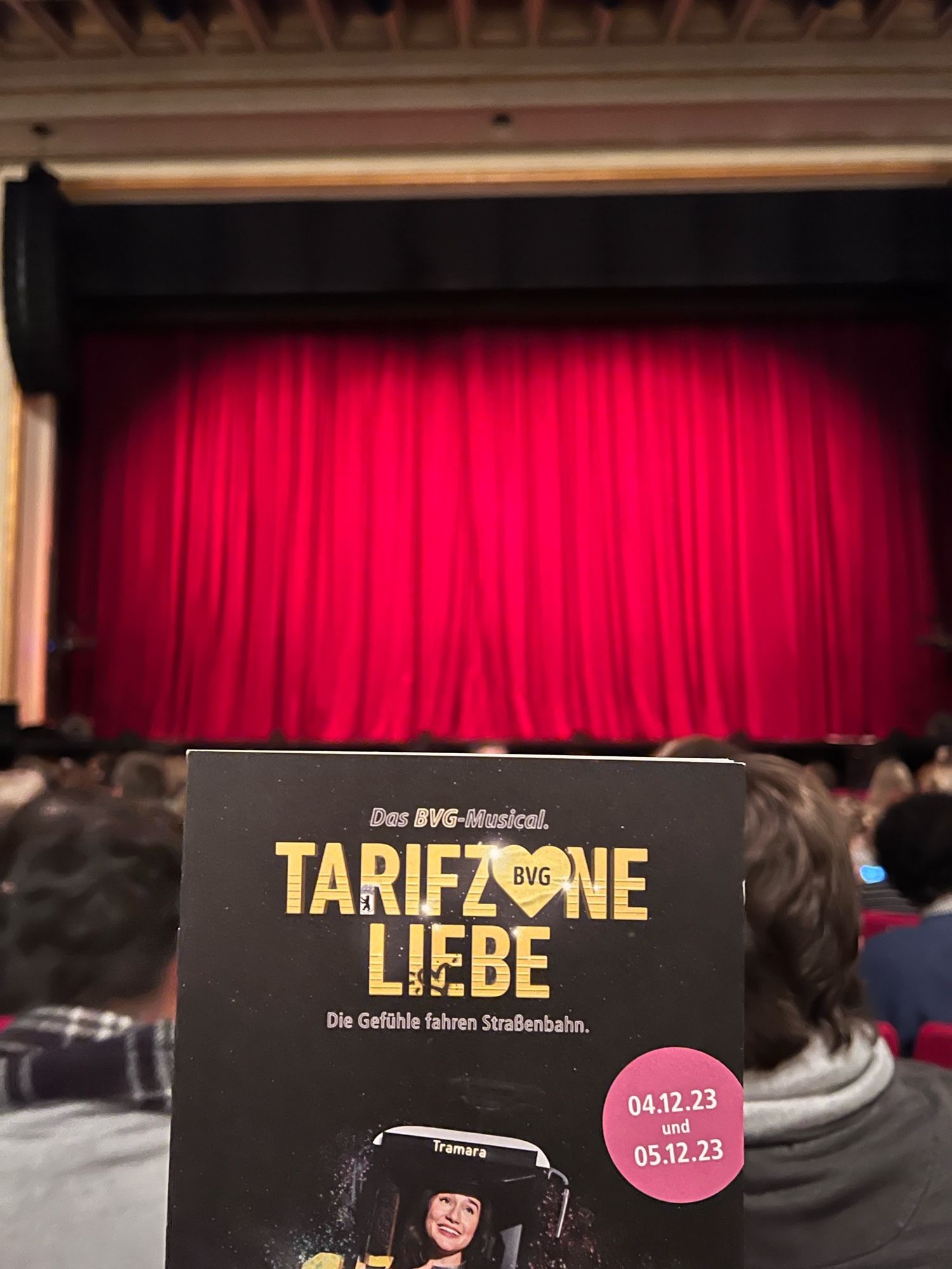 Der rote Vorhang im Admiralspalast. Davor das Programmheft zum BVG-Musical „Tarifzone Liebe“. Das O in Zone ist ein Herz, in dem „BVG“ steht.