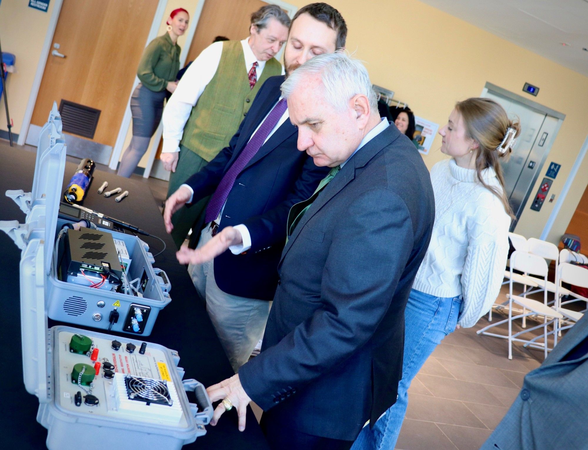 Senator Reed and Professor Singley standing next to and talking about a few pieces of portable field science equipment displayed on a table.