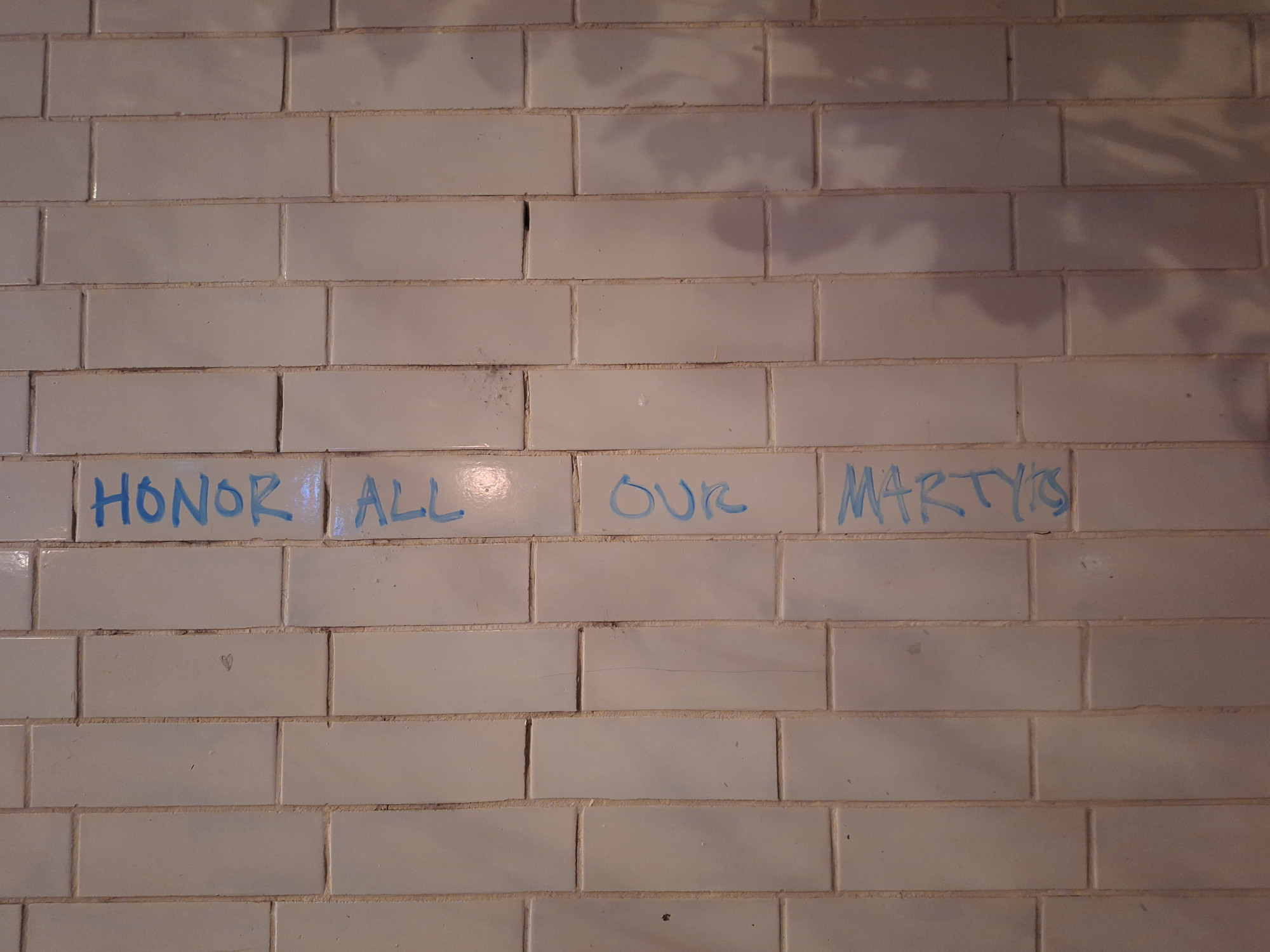 White brick wall with text on it saying "honor all our martyrs"