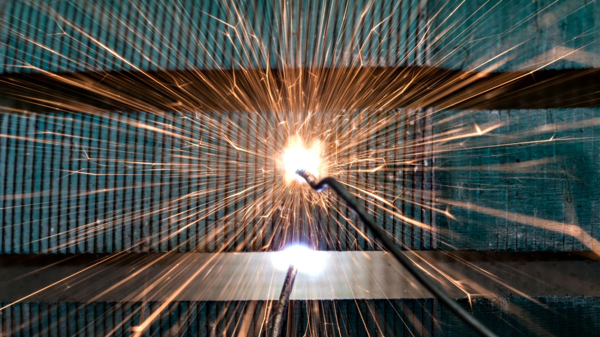 A macro photo of a high voltage electrical spark firing in a fireworks like pattern against the green striped background of a motor armature which the spark was triggered on.