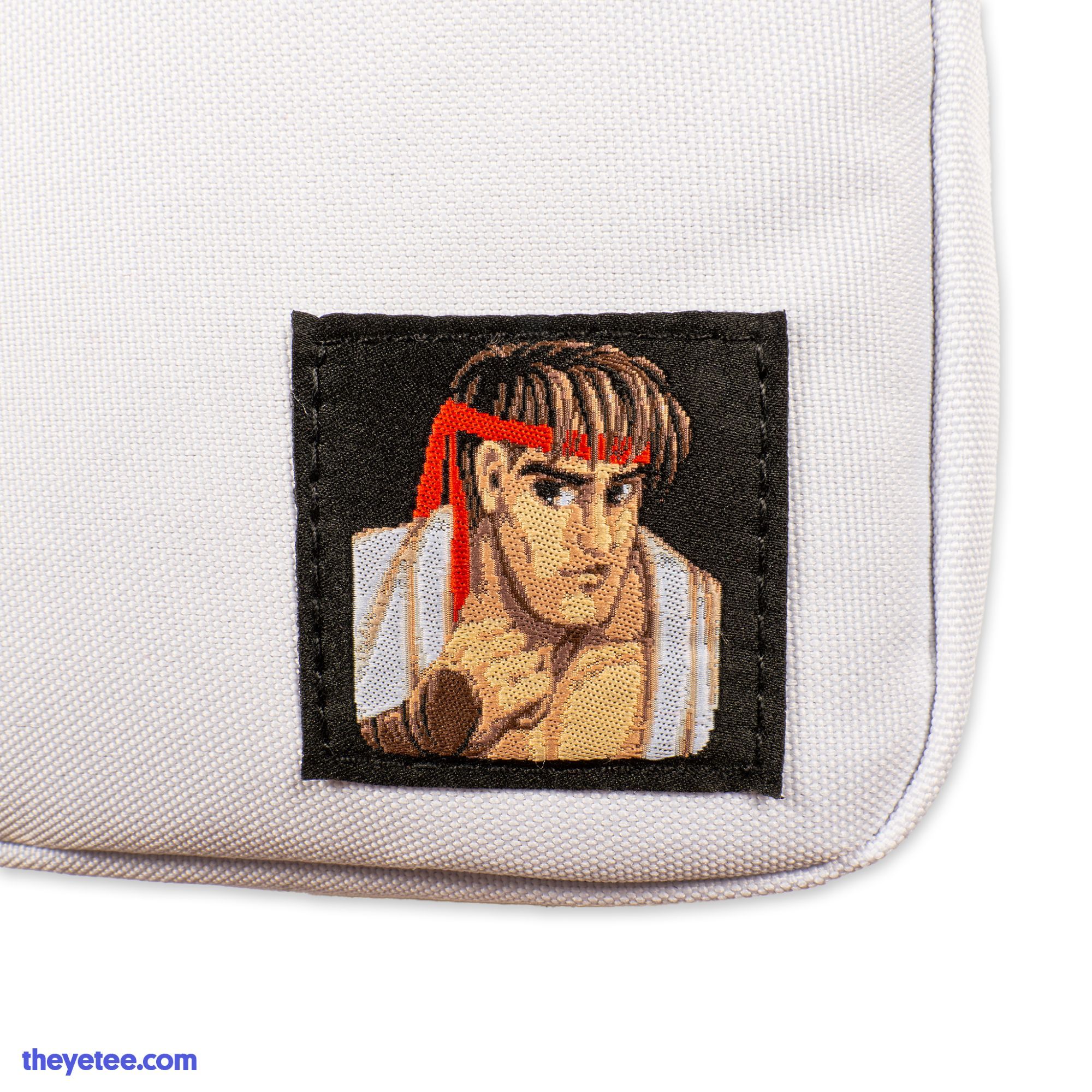 A front photo of a White Street Fighter 2 Ryu shoulder satchel. There is a square patch of Ryu's fighter icon in the bottom right corner.