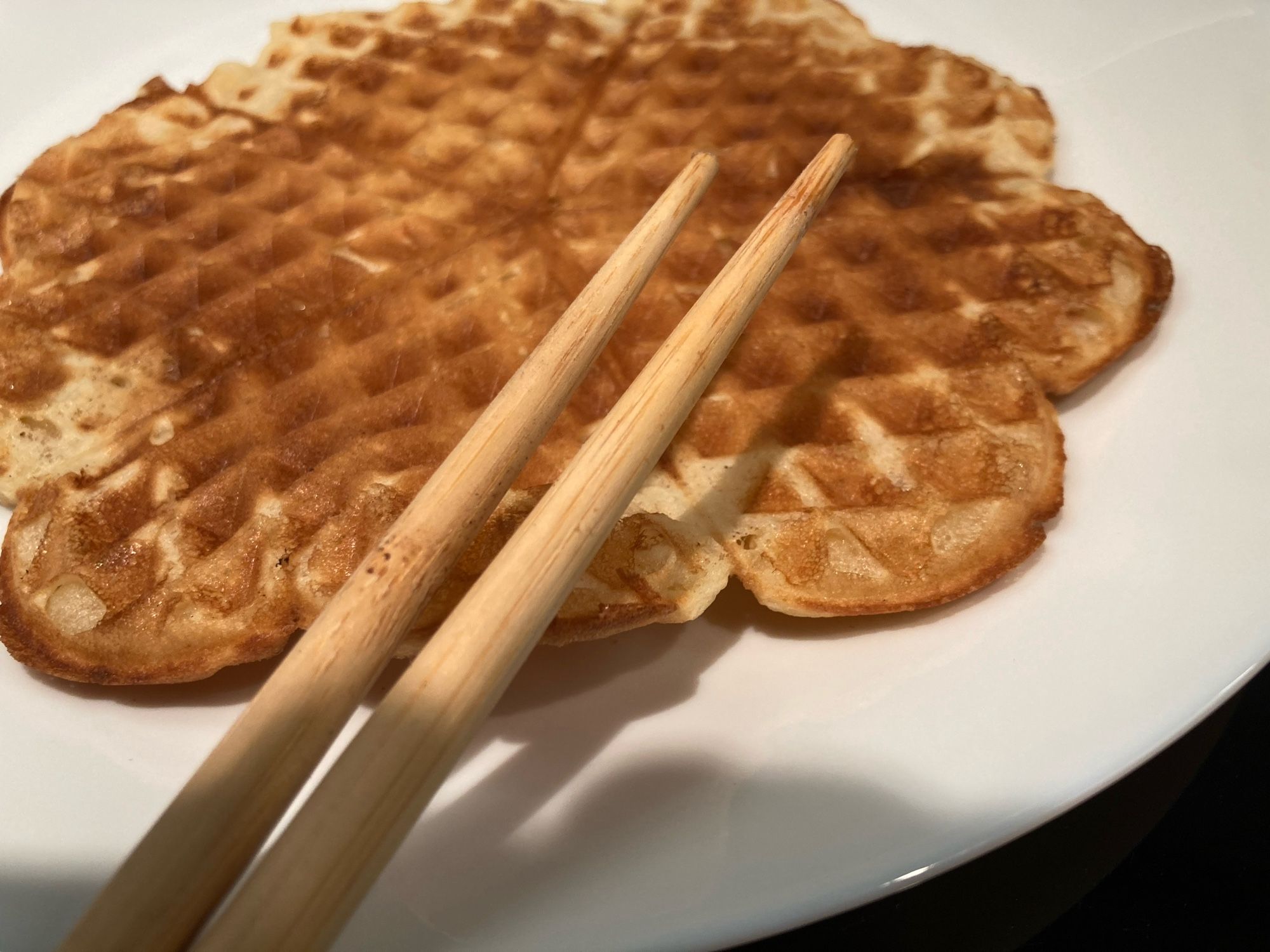 Eine gebackene Waffel auf einem Teller liegend. Stäbchen sind am Teller angelehnt.