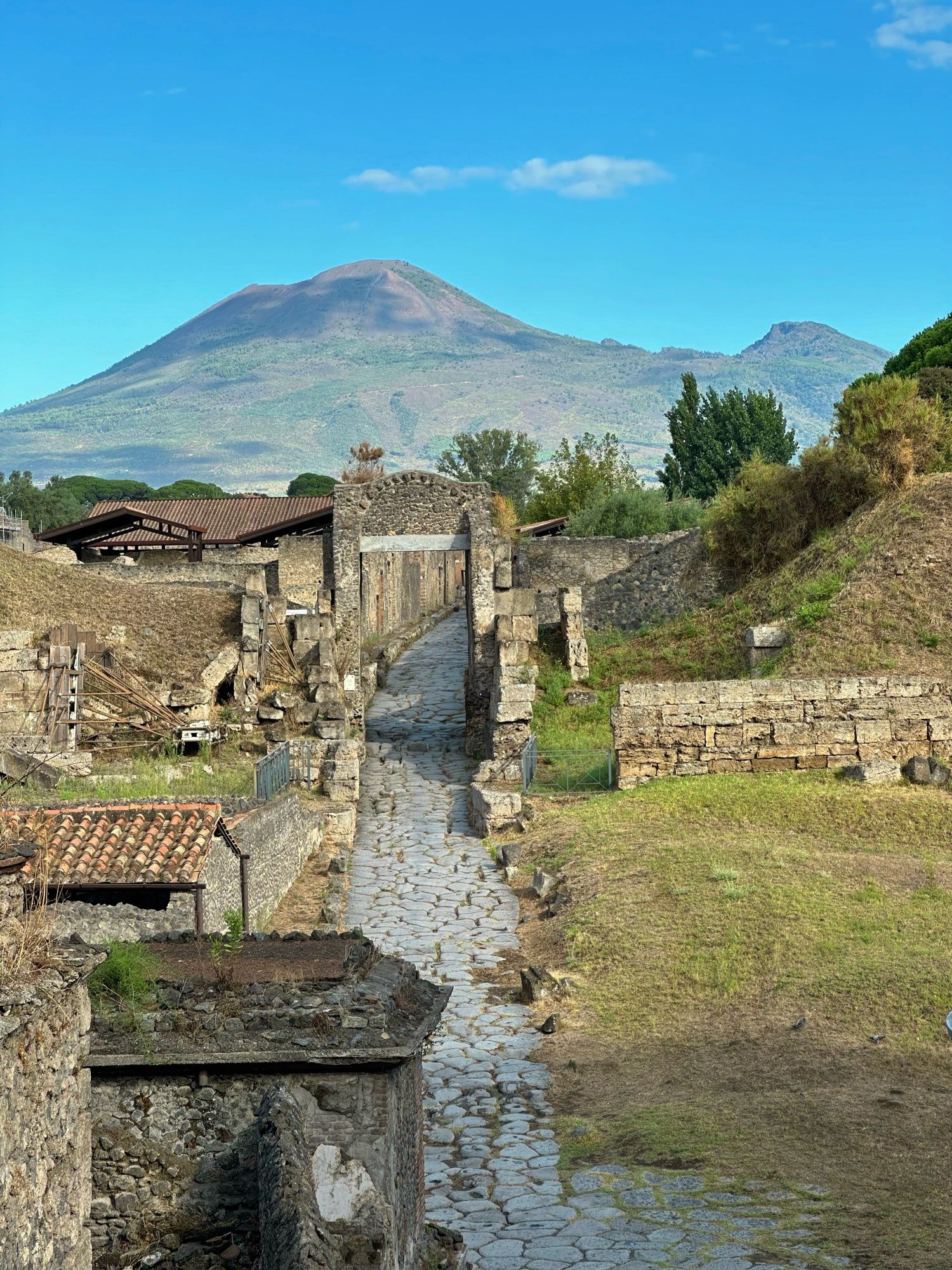 View up through the Nocera gate with the paved road wending its way into the city. Vesuvius is dappled in sunlight and the sky is a light blue with a couple of white wispy clouds.