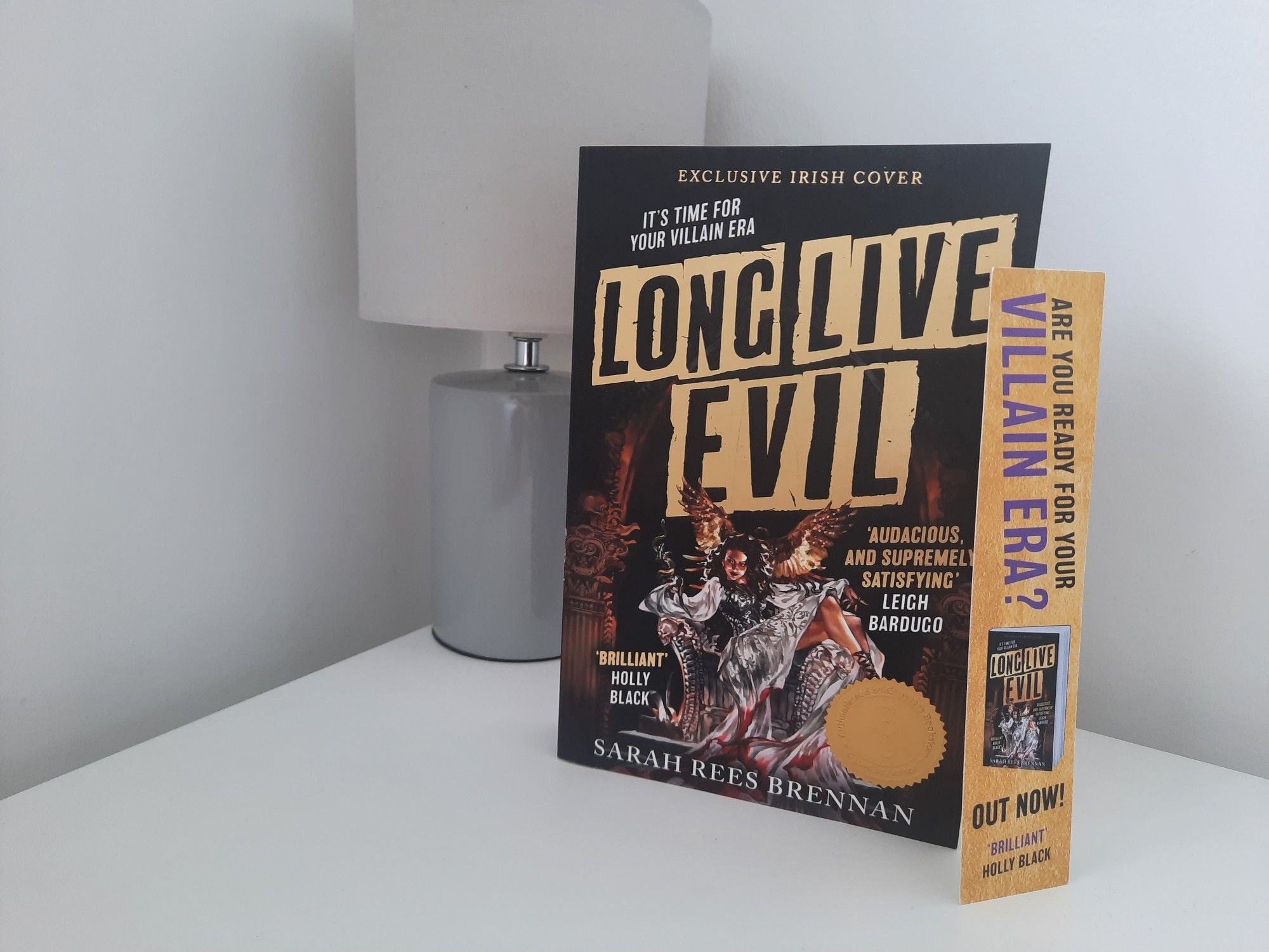 Long Live Evil by Sarah Rees Brennan book resting on a white bedside locker with a grey lamp behind it.