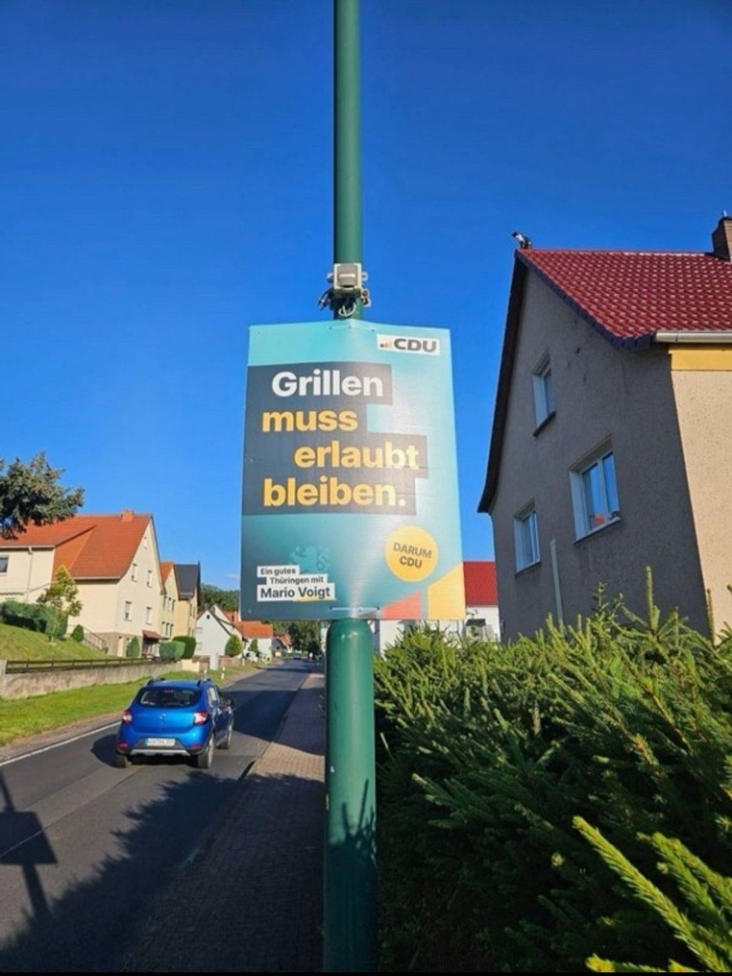 Das Foto zeigt eine Straße mit zweigeschossigen Häusern. Am Straßenrand steht ein Laternenmasr, an dem ein CDU-Wahlplakat mit folgendem Text hängt:
CDU
Grillen muss erlaubt bleiben.
Darum CDU 
Ein gutes Thüringen mit Mario Voigt