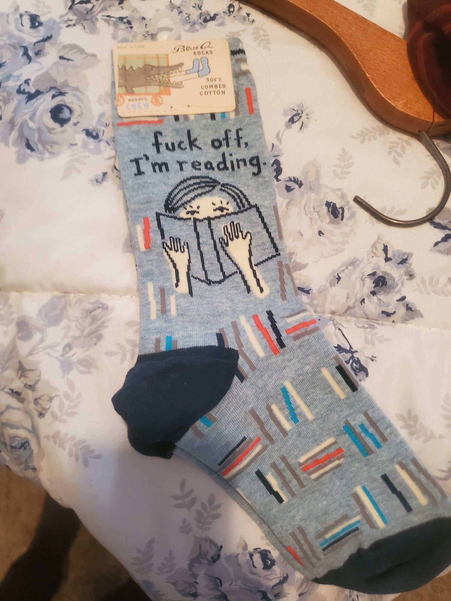 A pair of light blue socks with an illustration of someone peaking over a book. Text says "fuck off I'm reading"