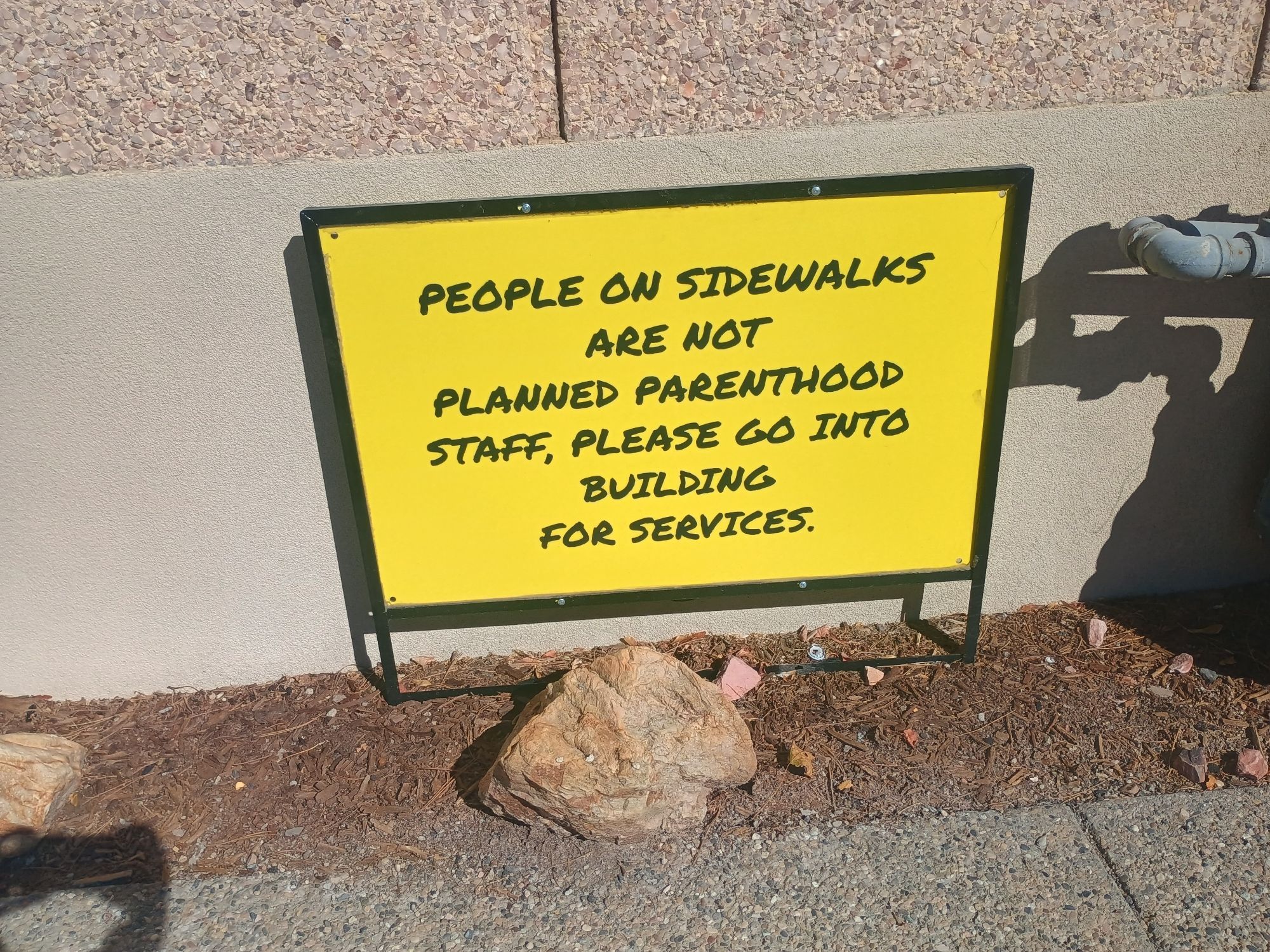 a yellow sign with black text saying "people on sidewalks are not planned parenthood staff, please go into building for services"