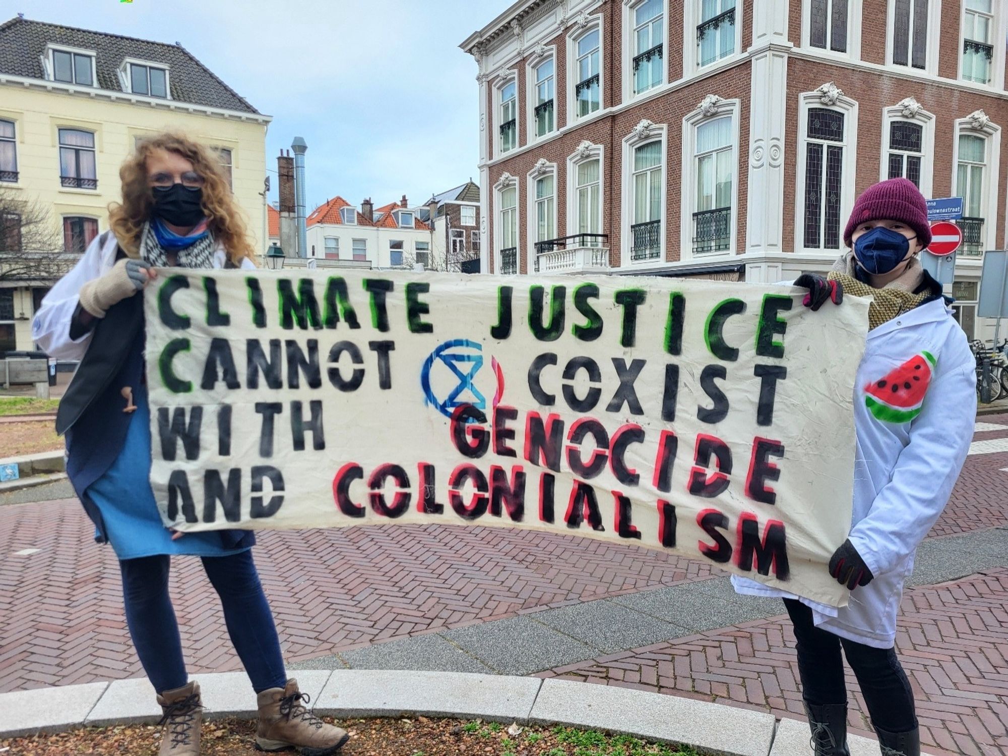 Two Scientist Rebels holding a banner that says: Climate Justice cannot coexist with genocide and colonialism