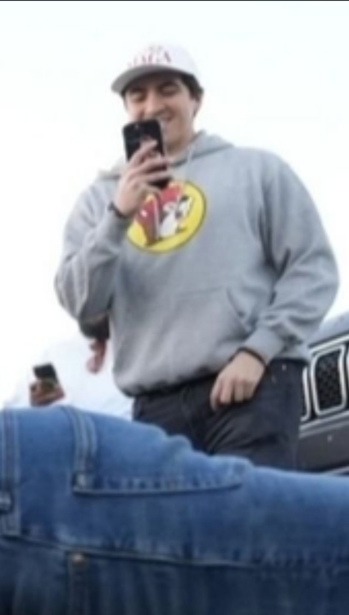 A close crop of the previous photo showing detail of a goober in a buccees sweatshirt recording vertical video of Jacob Tampa warming up