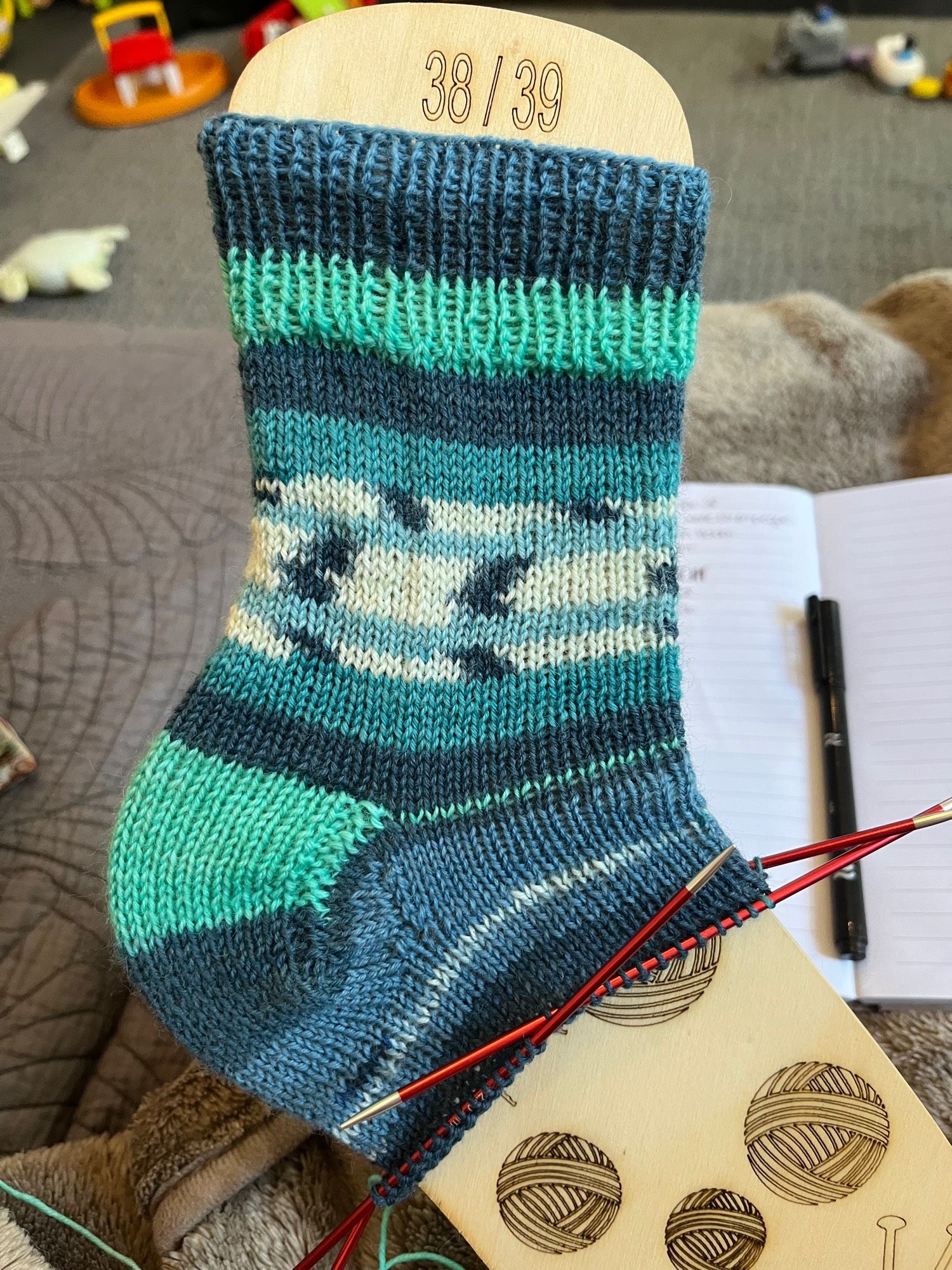 Eine zur Hälfte fertig gestrickte Socke in verschiedenen Blautönen.