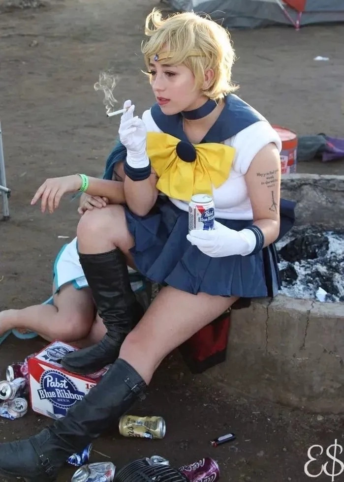 A Sailor Uranus cosplayers sitting on a firepit drinking a Pabst Blue Ribbon, smoking a cigarette, and starring into the middle distance