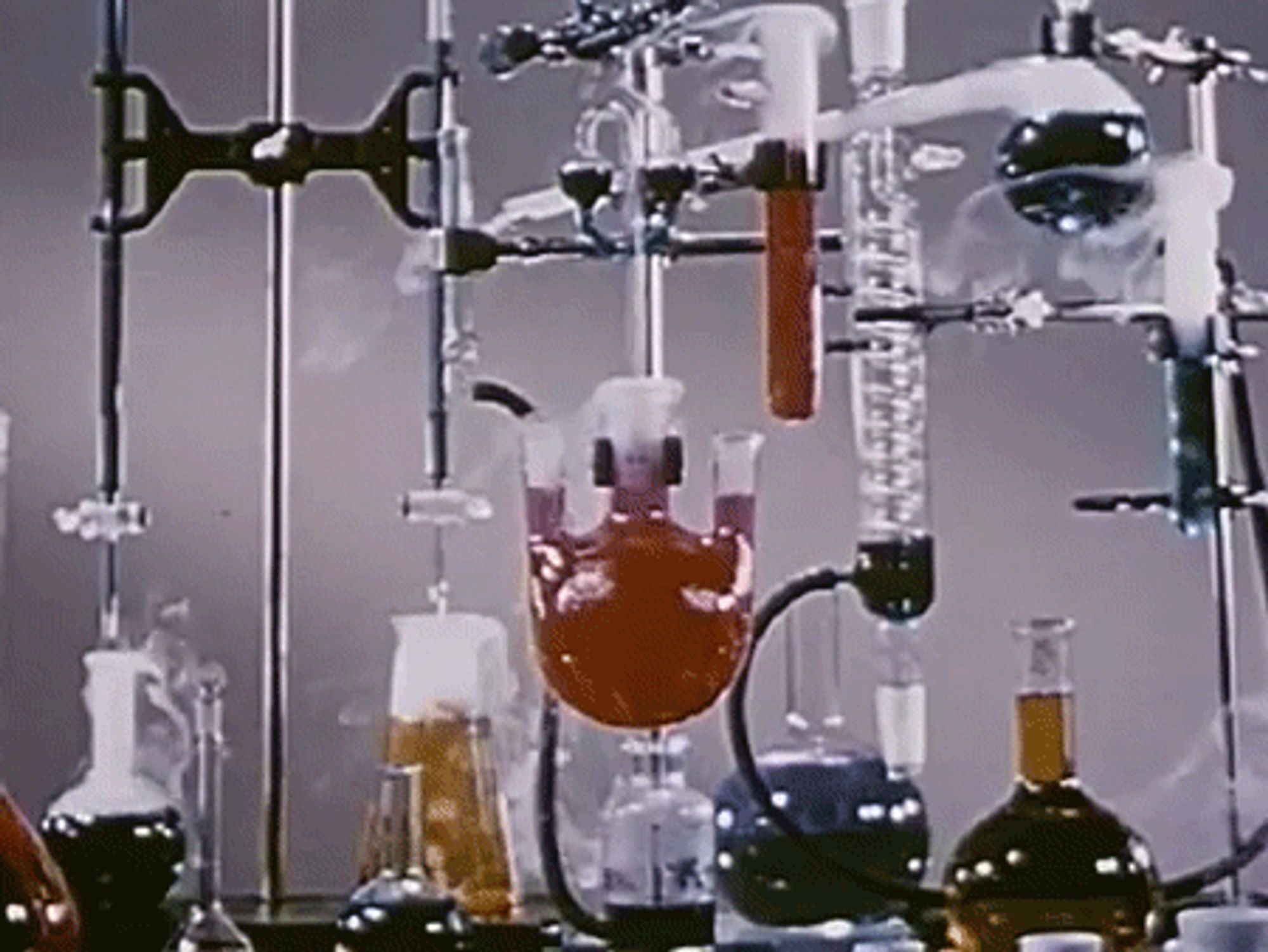 Animated GIF of a chemistry lab rack set up with various flasks and cylinders boiling and putting out smoke, in that cliched mad scientist fashion.