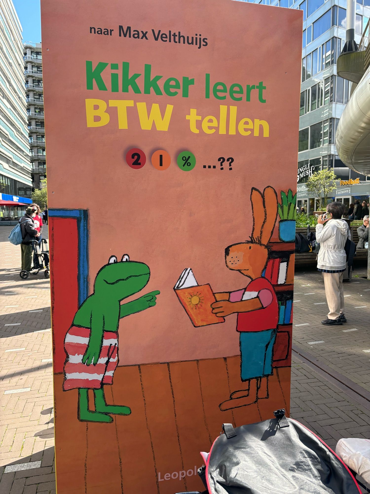 Boek van ruim 2 m van Max Velthuijs met de titel “kikker leert BTW-tellen” met daaronder een cartoon van kikker met een rood-wit gestreepte broek en haas met een boek in de hand, rood shirt en blauwe broek.