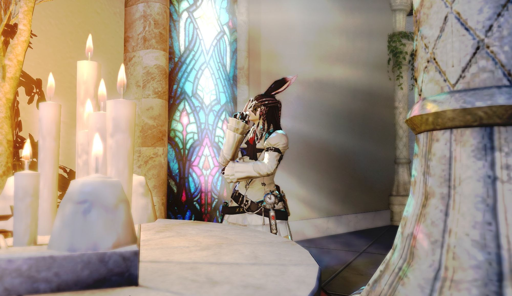 An original video game character, a male viera from Final Fantasy XIV, is standing by a stained glass window with light shining in through it. He is dressed in a white longsleeve shirt with two leather belts around his waist, a black bowtie, a leather armband around his left arm, and black and white gloves. He has his right hand up near his mouth, in a "thinking" position. He is wearing a gold and black mask over his eyes. He has long brown hair with purple to white tips and braids on either side of his face, his bunny ears are also dark brown with purple to white tips. In the foreground of the photo, there is a large cement pillar on the right, 7 lit candles on the left, and a few plants on either side.