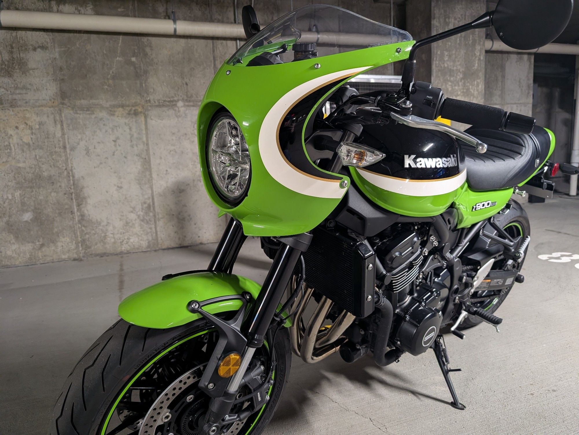 A green and black Kawasaki motorcycle, sitting on its kickstand in an underground garage