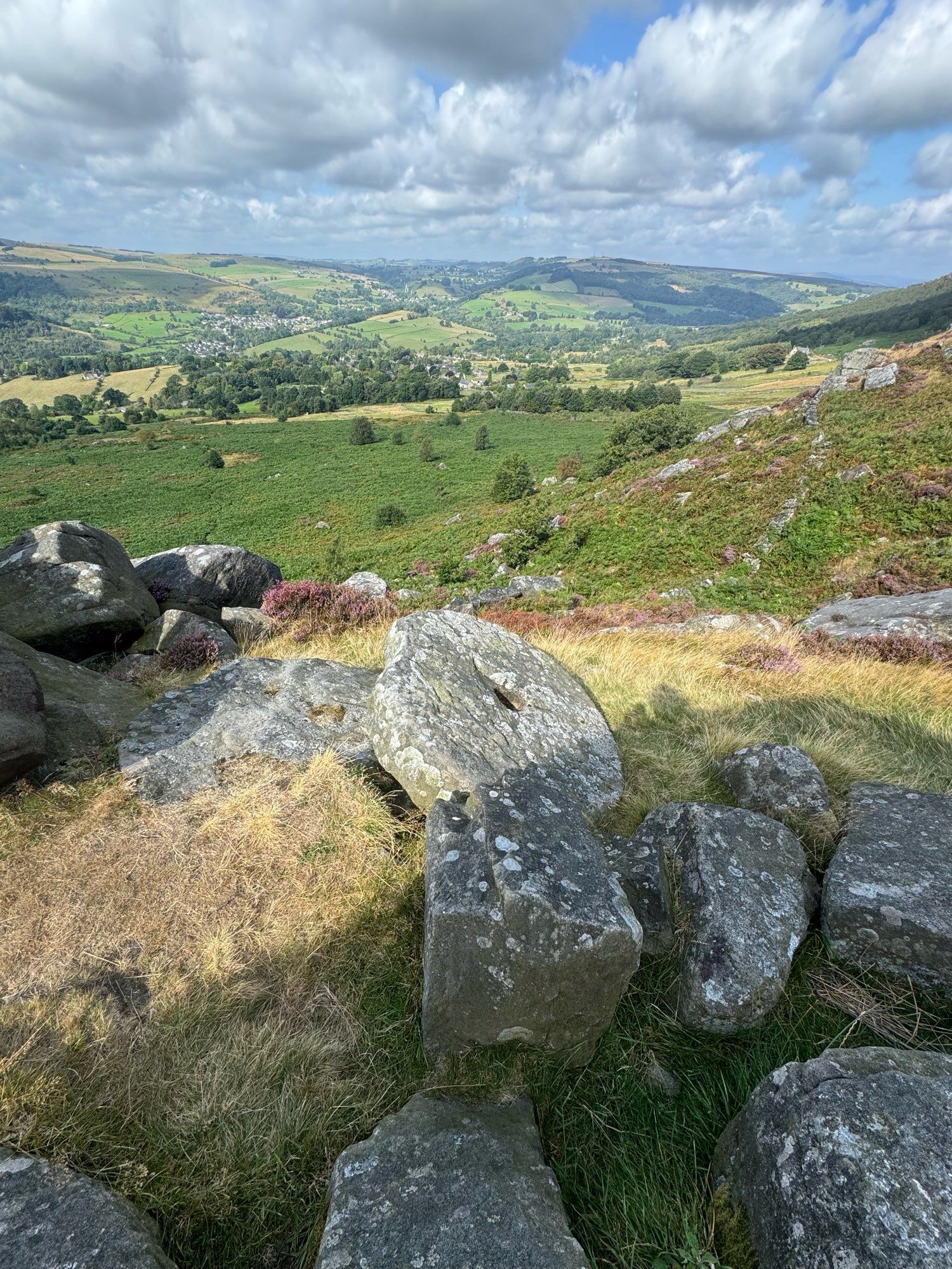 Abandoned millstone on Curbar Edge. Rolling hills of the Peak District and Derwent Valley in the background