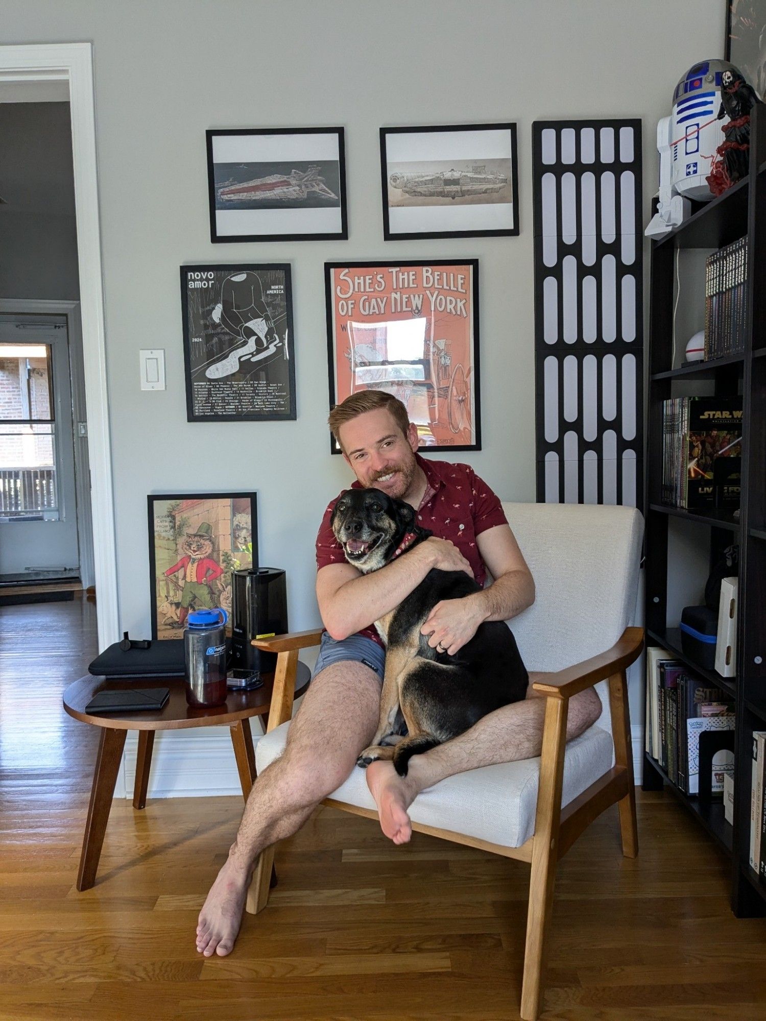 Jake and his dog freyja sitting together in a chair. He is in shorts and a red shirt. The dog is looking at the camera