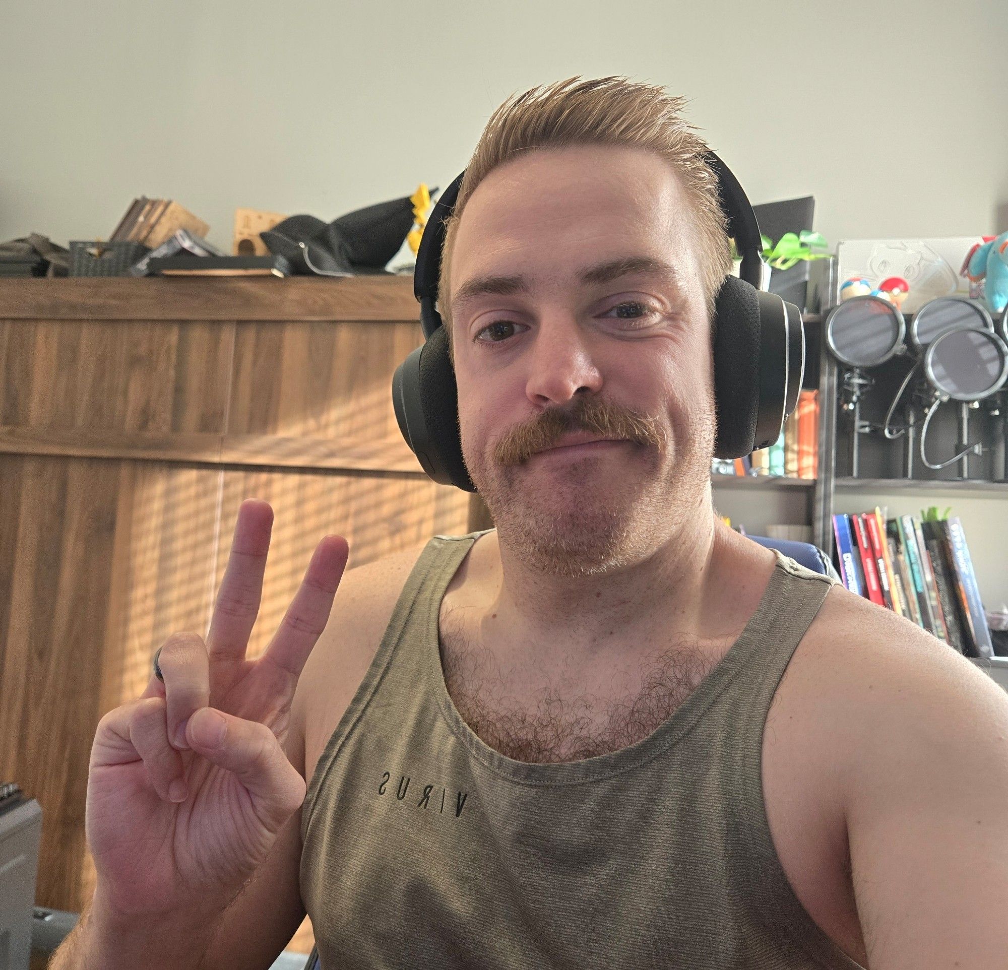 Selfie of Jake wearing gaming headphones in a tank top. He is doing the peace sign.