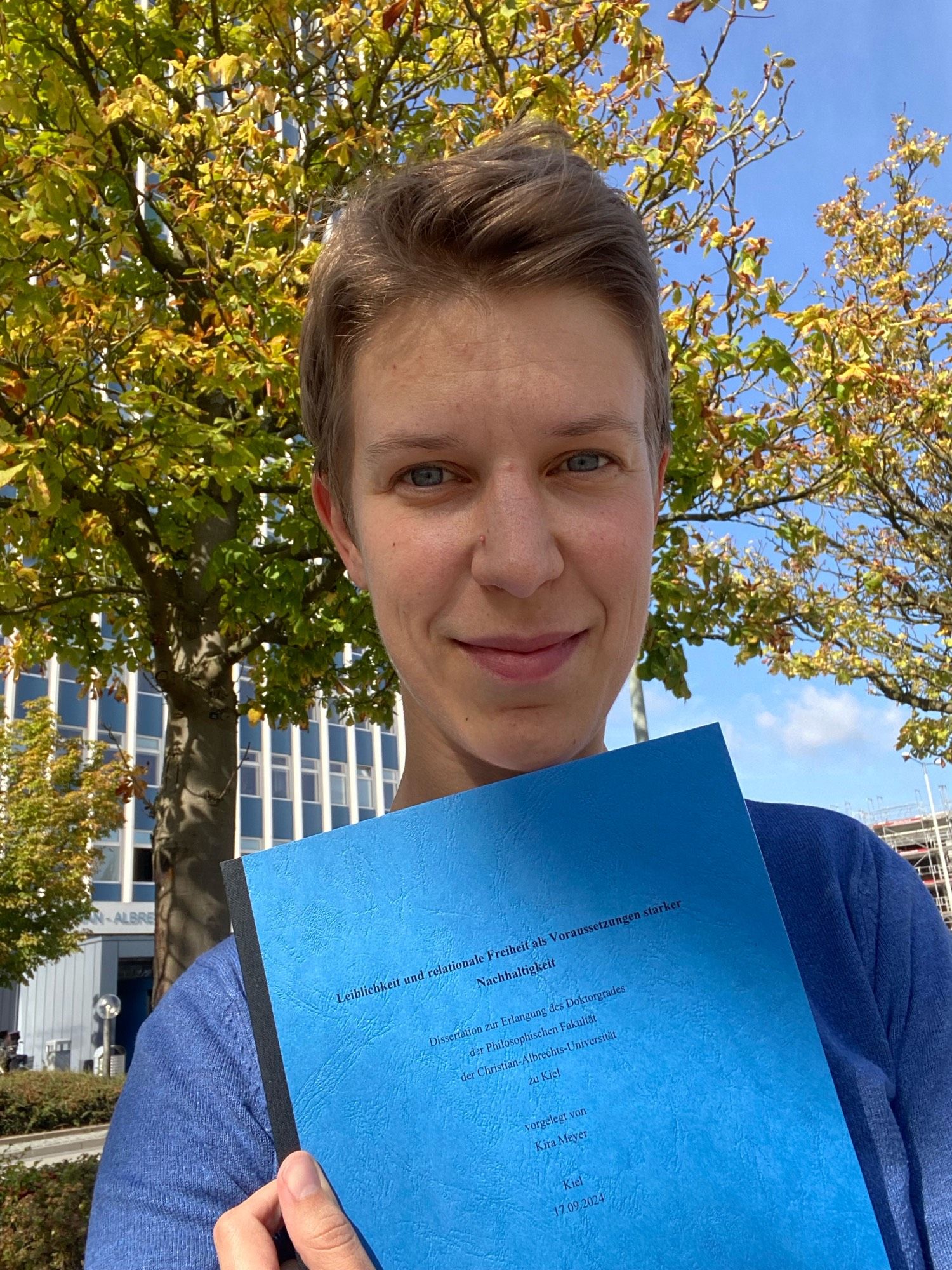 Me holding a copy of my dissertation, standing in front of the tower of Kiel University