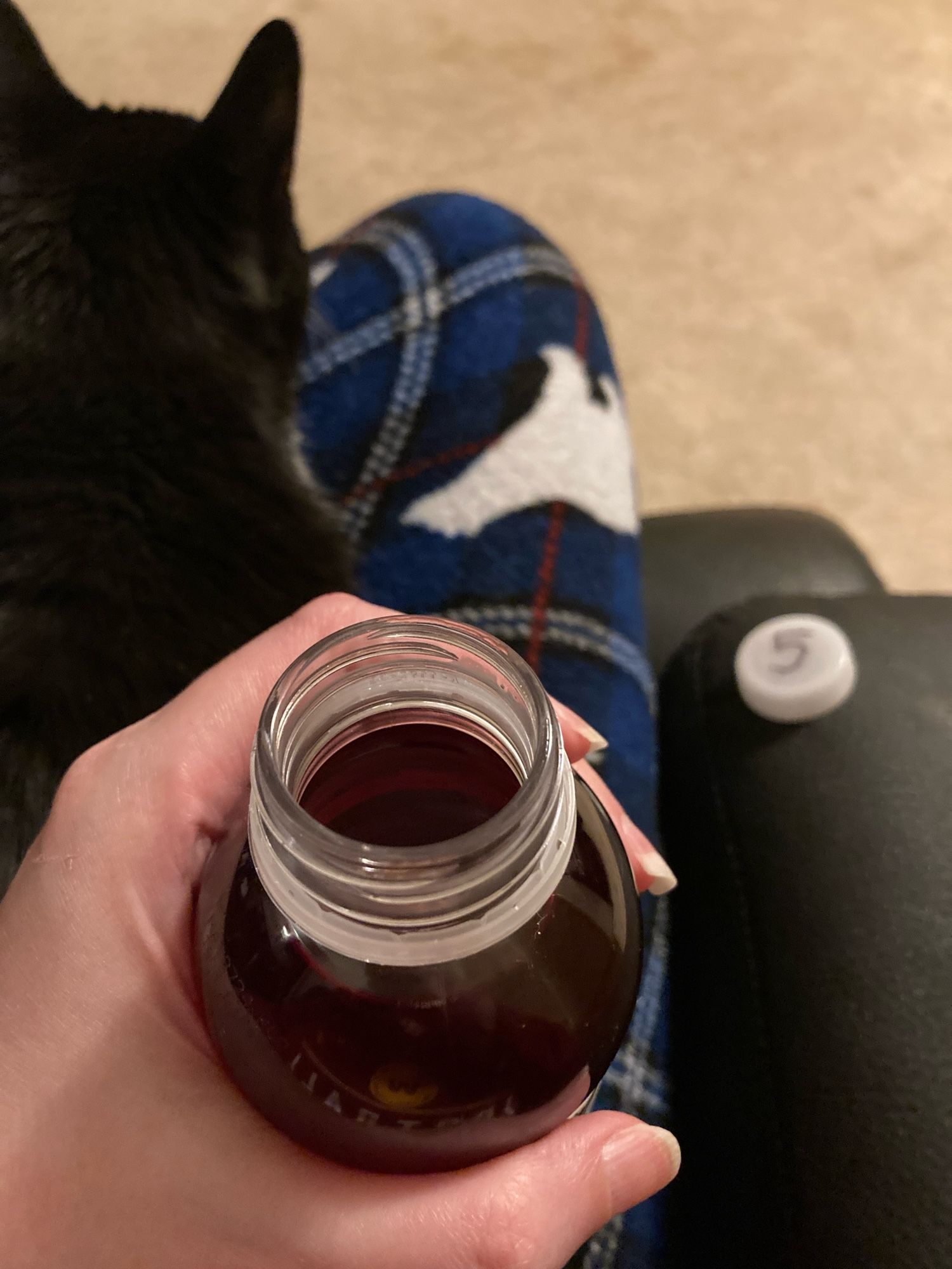 sleepyhead holding an open bottle of VitaminWater XXX. A nearby bottle cap reads “5”. Also, she has a cat on her lap.