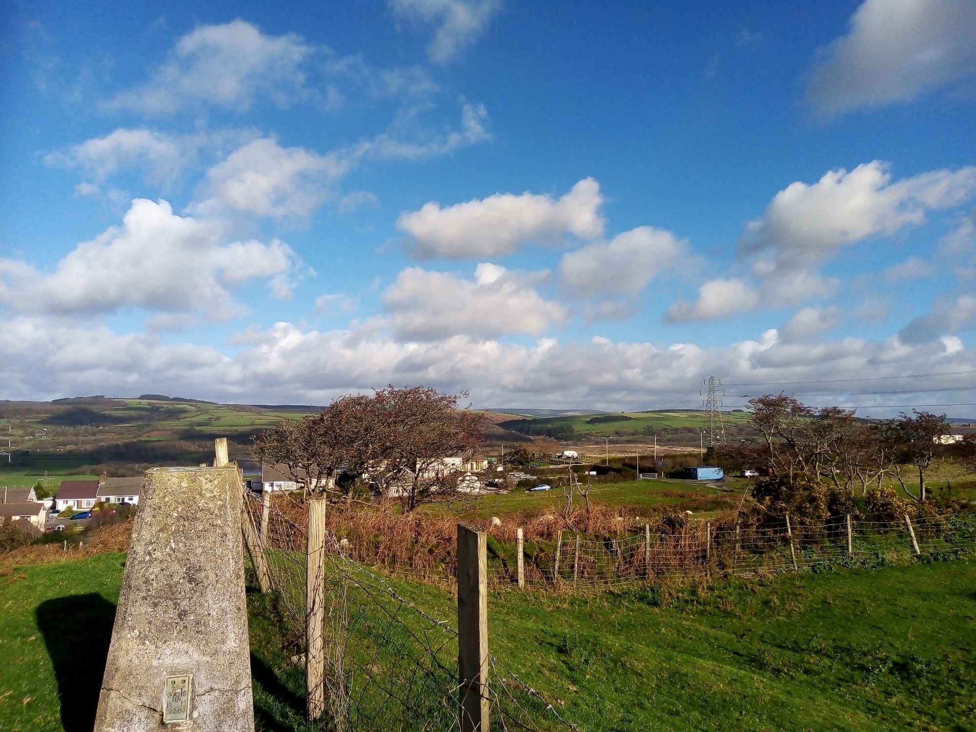 Landscape with clouds against blue sky. Lower left is a Hotine pillar or trig point