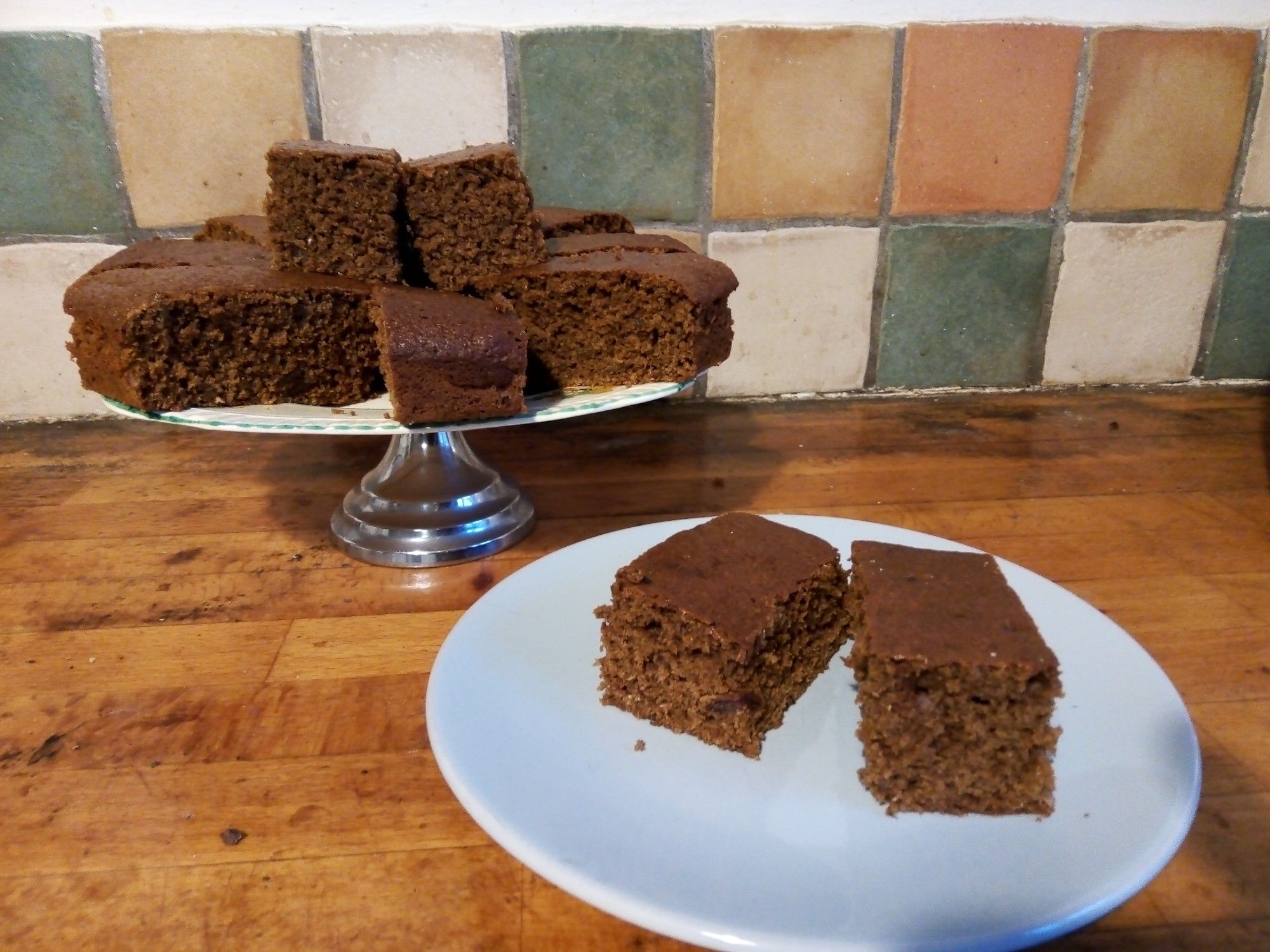 Plate of Gingerbread in background with2 pieces on small blue plate to right foreground .