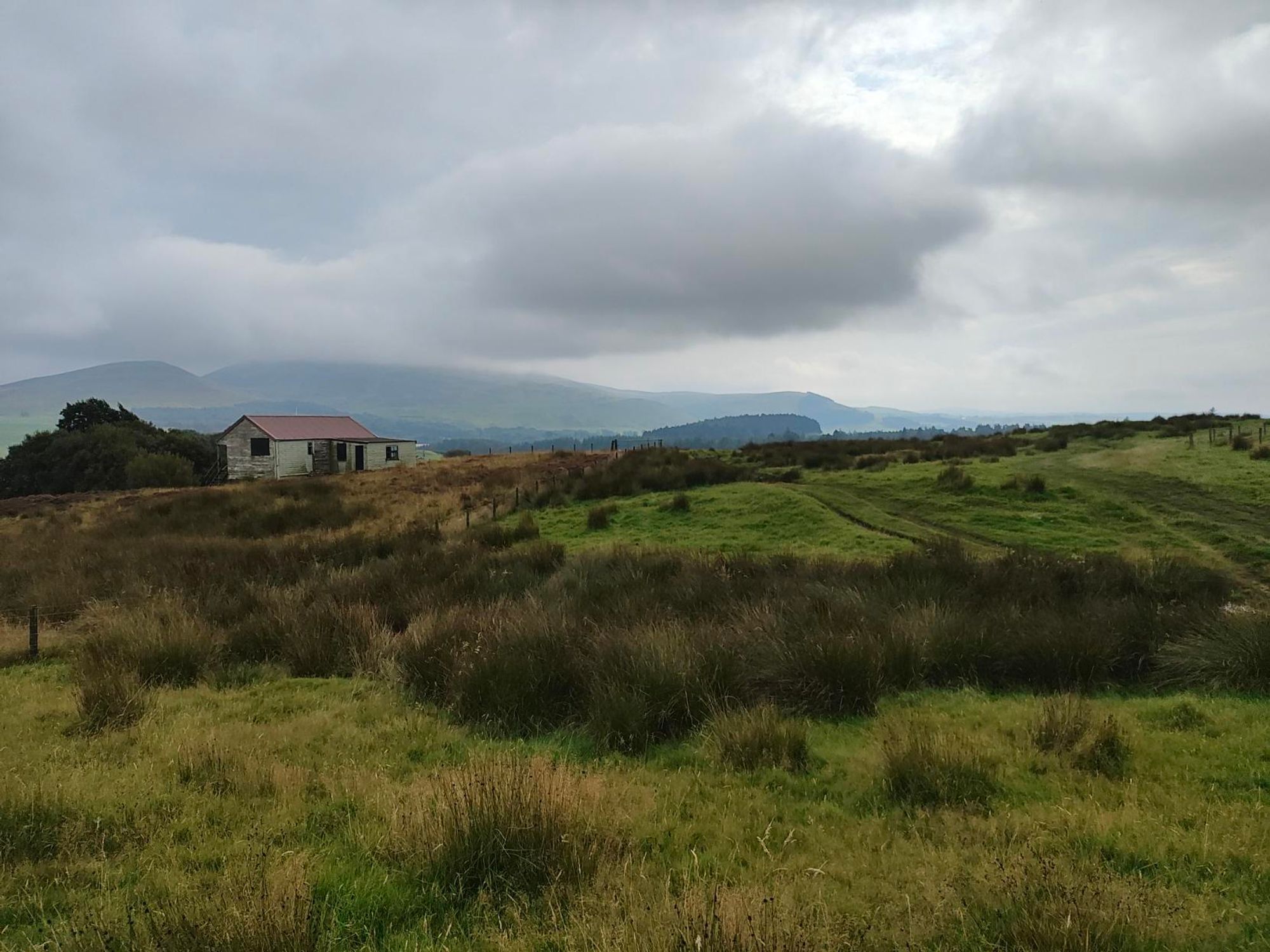 Empty moorland with an old wooden house and hills In distance. Low clouds