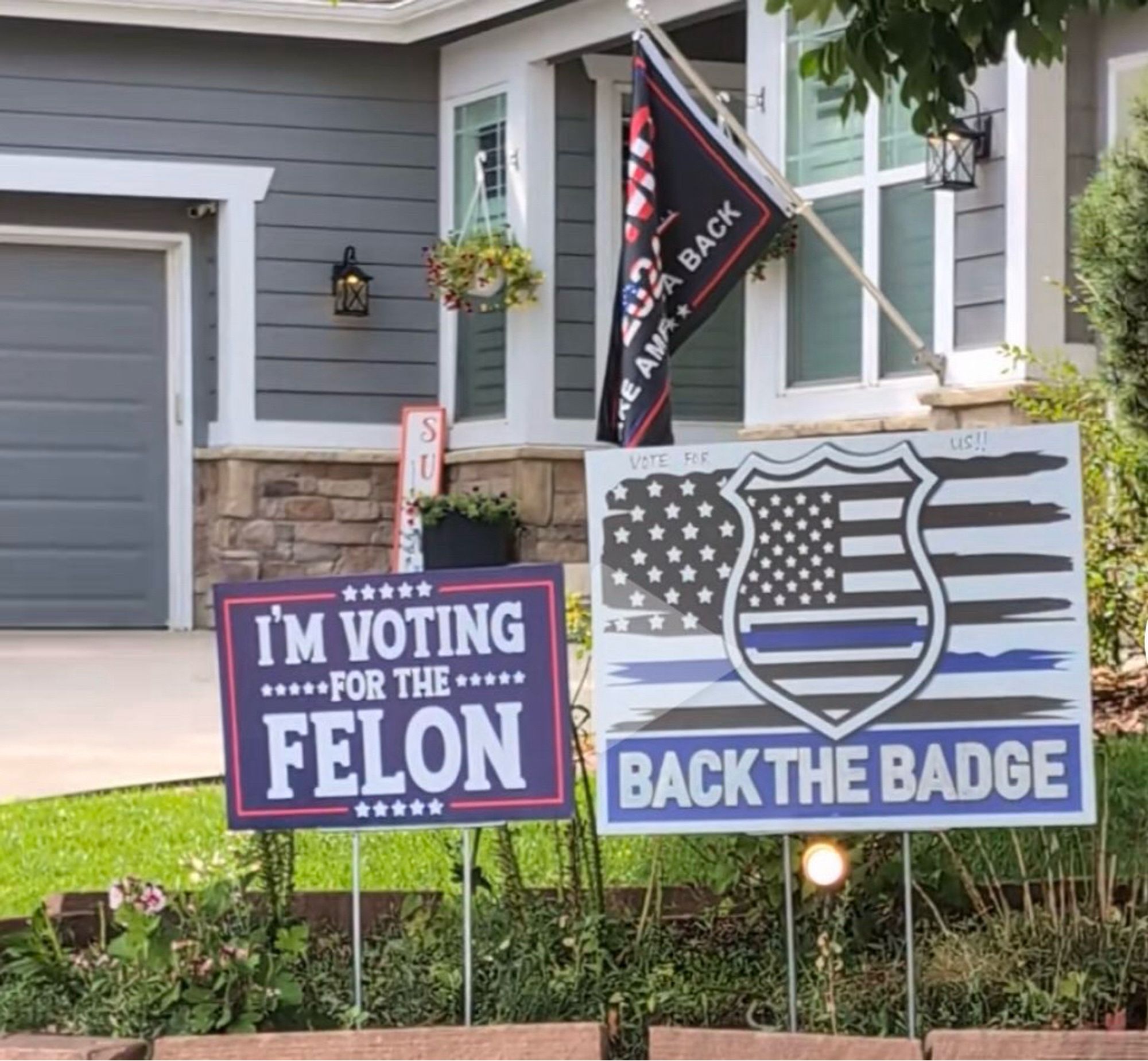 A picture of a front yard with three different Maga signs one that says Maga 2024 take America back one that says I’m voting for a felon and one that says back the badge with a thin blue line flag