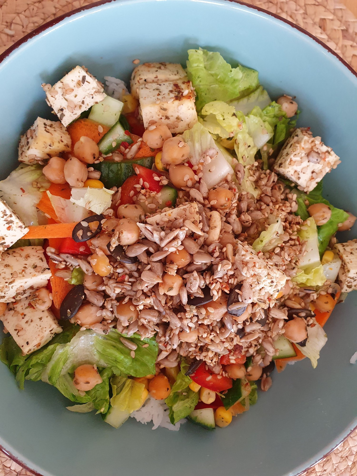 Der Salat auf einem Reisbett mit Tofu-Kichererbsen-Sämereien-Topping in einer taubenblauen Steingutschüssel von oben fotografiert 