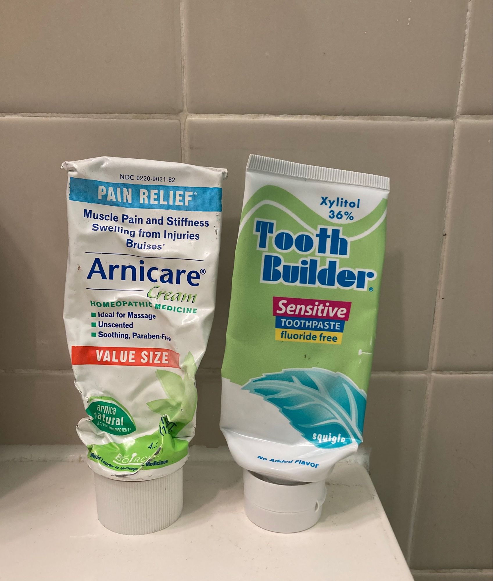 Standing tube of Arnica cream next to a standing tube of toothpaste that are the same shape/size and have an unfortunately similar color scheme