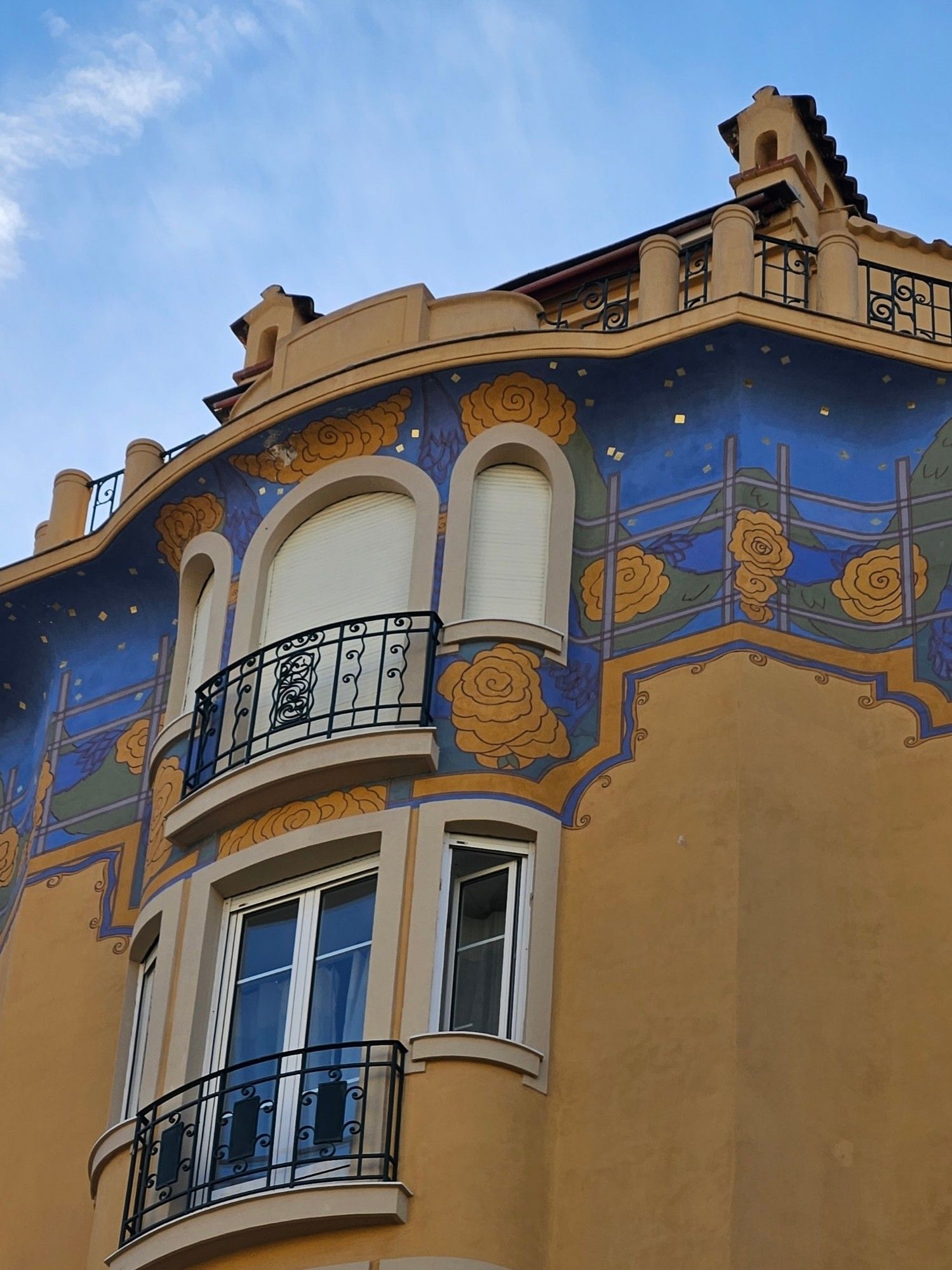 The upper storey of a building painted ochre. It has arched windows and a frieze of flowers painted blue.