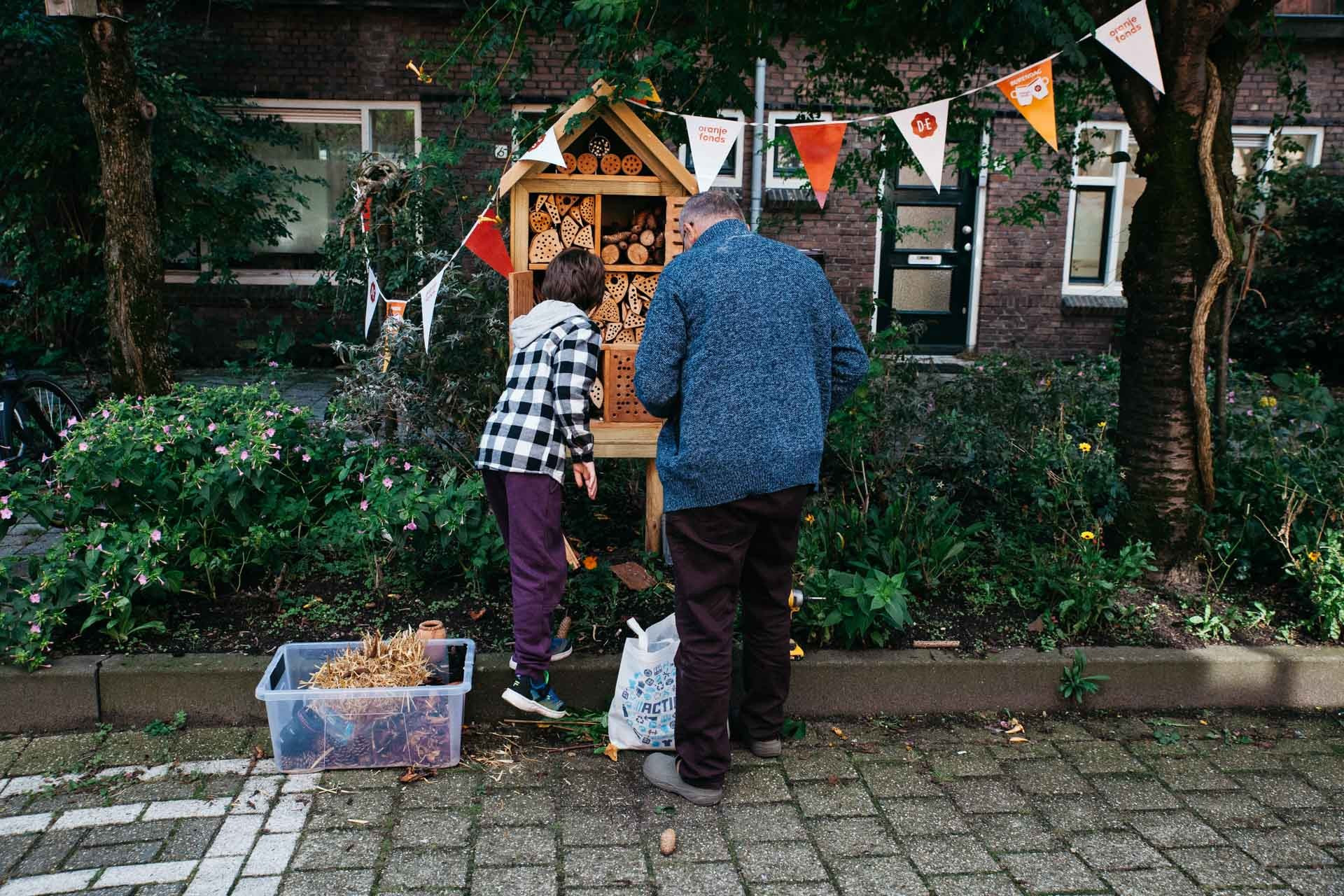 Een man en een kind vullen een insectenhotel met takken, blaadjes, stro en dennenappels tijdens burendag.