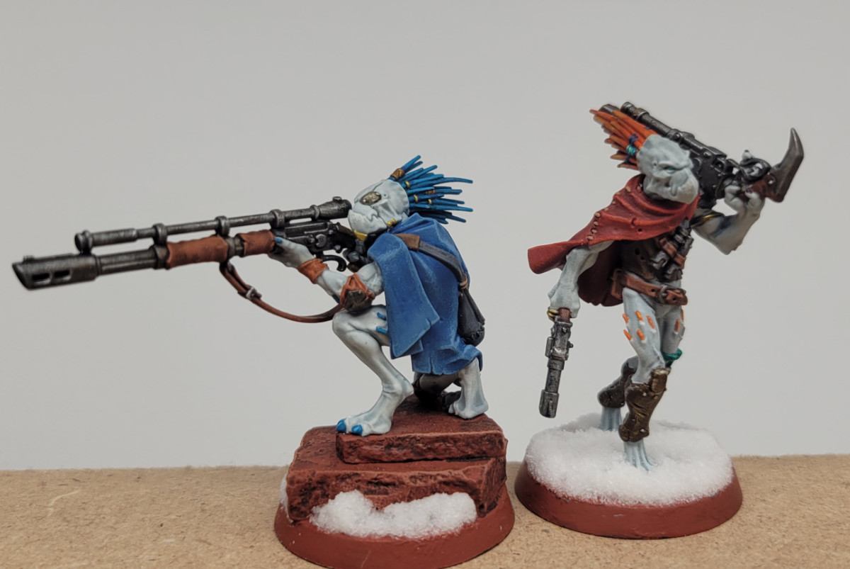 two painted kroot minis from warhammer 40k. left is perched on some red rocks with a longass gun, right is walking through snow very nonchalantly with a shotgun and a pistol and looking hard as fuck. they both are extremely pale skinned, almost greyscale, and its super gross but in an endearing way.